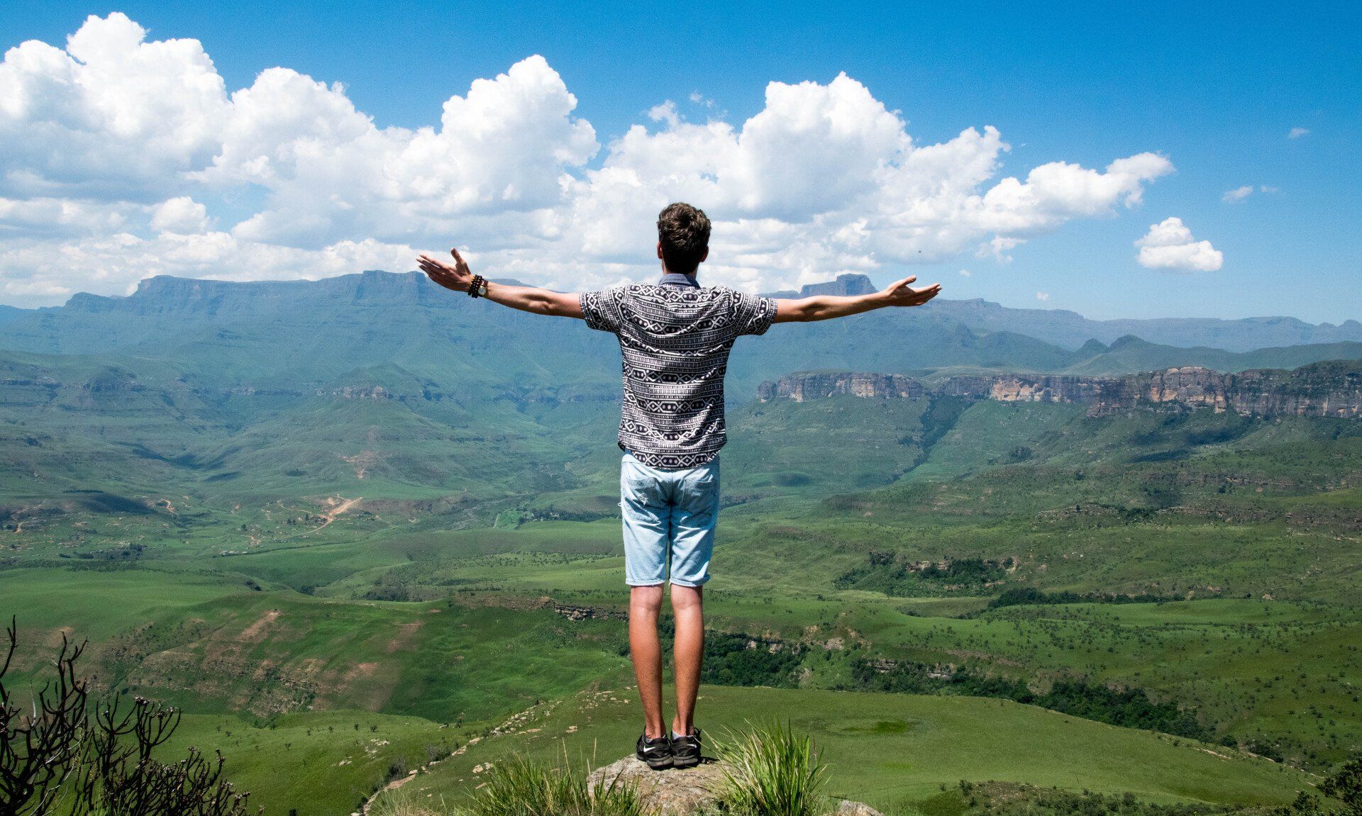 A man is standing on top of a mountain with his arms outstretched.