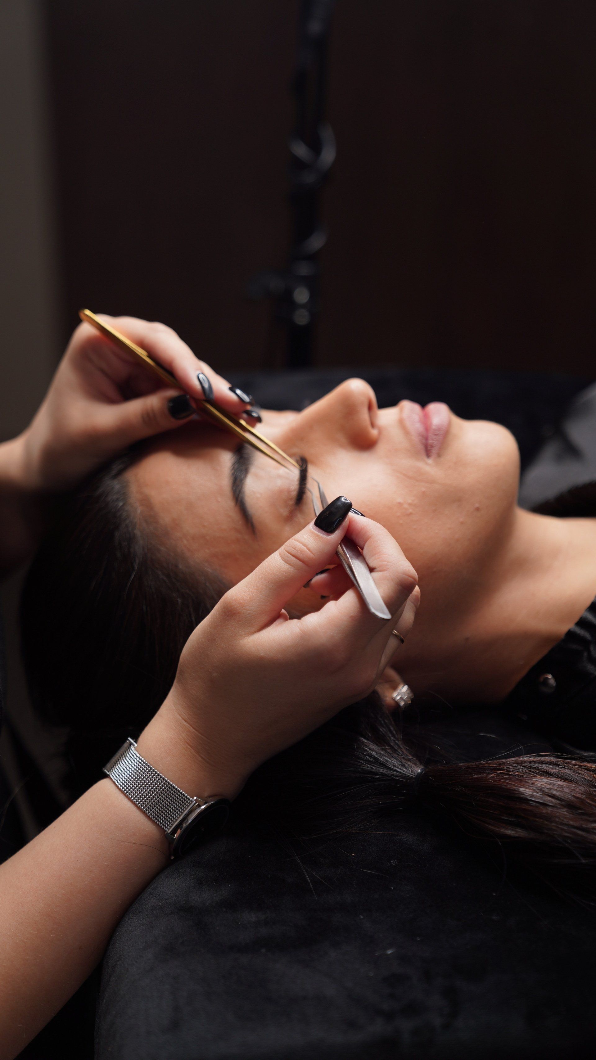 A woman is getting her eyebrows done by a makeup artist.