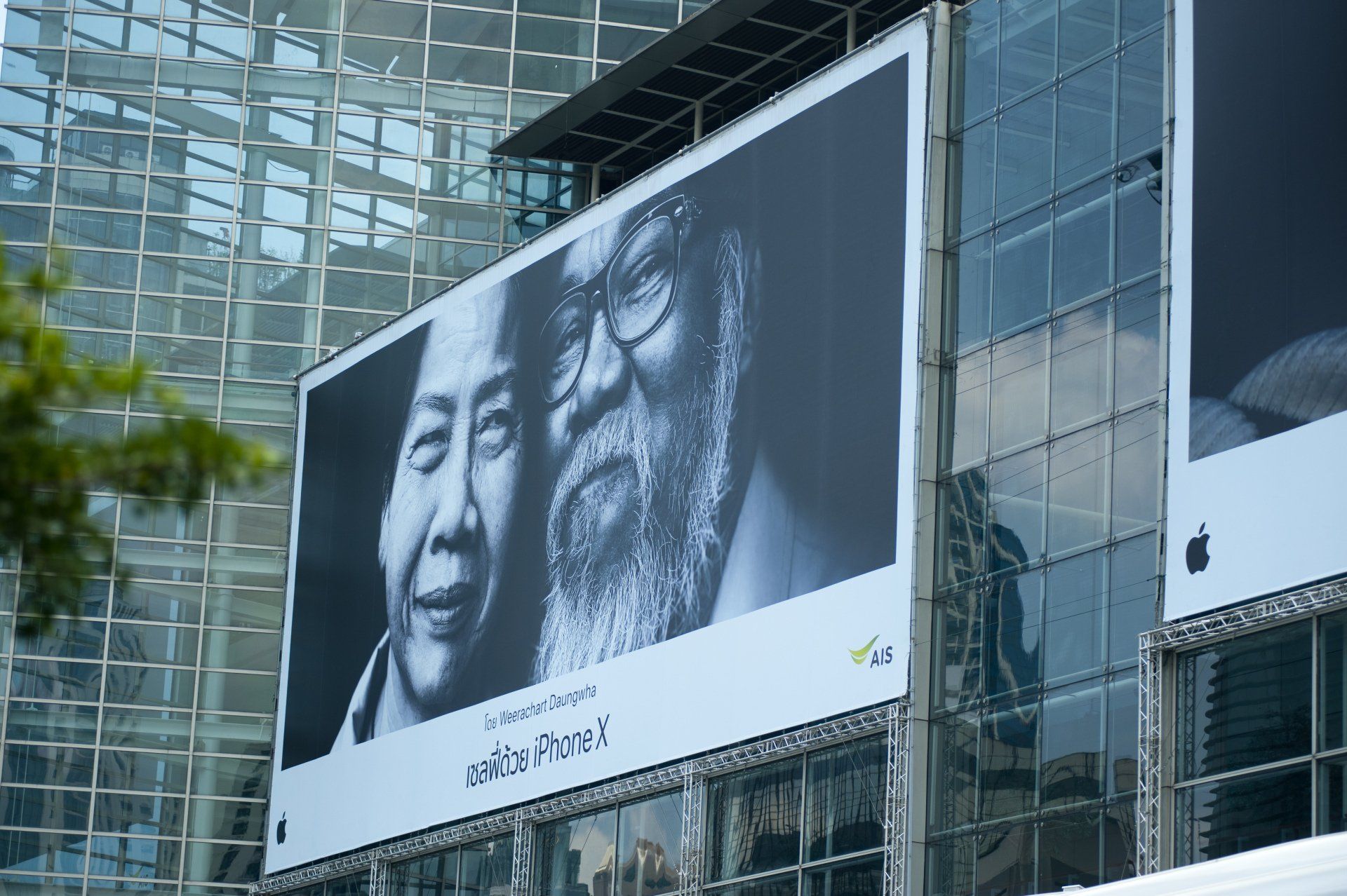 A large billboard on the side of a building shows a man with glasses and a beard.