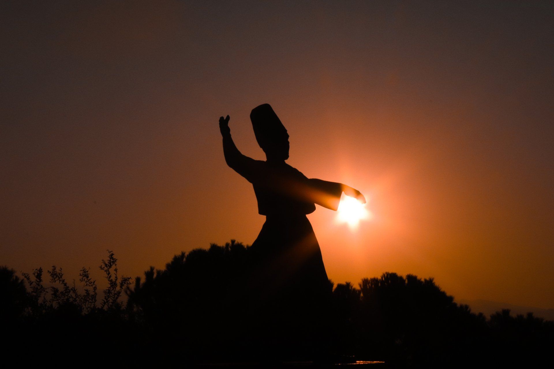 A silhouette of a person dancing in front of the sun at sunset.