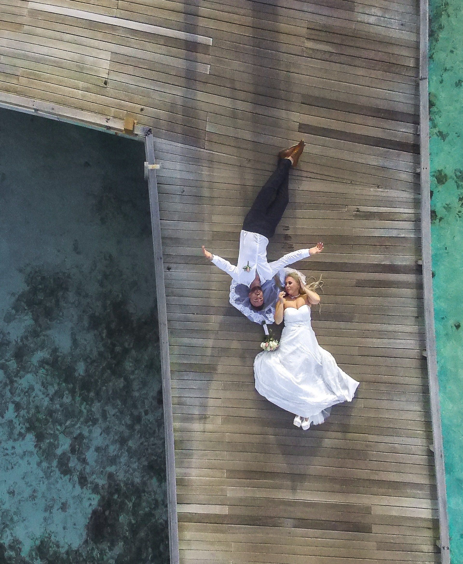 An aerial view of a bride and groom laying on a wooden dock.