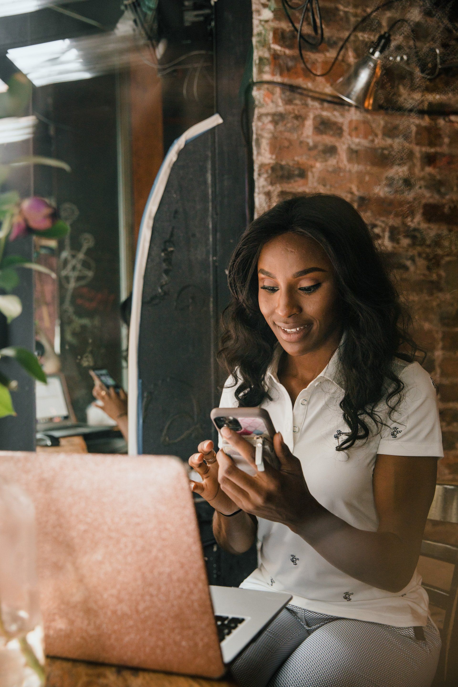 A woman is sitting at a table using a laptop and a cell phone.