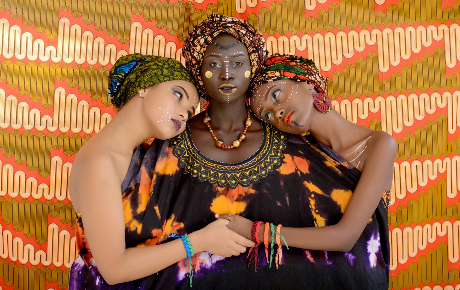 Three women are posing for a picture in front of a patterned wall.