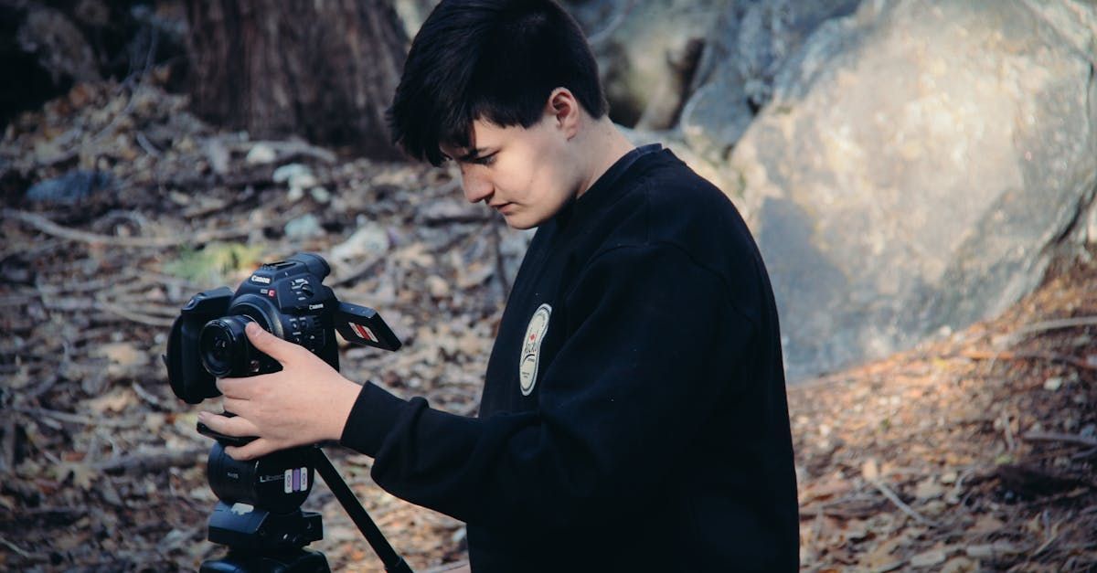 A young man is taking a picture with a camera in the woods.