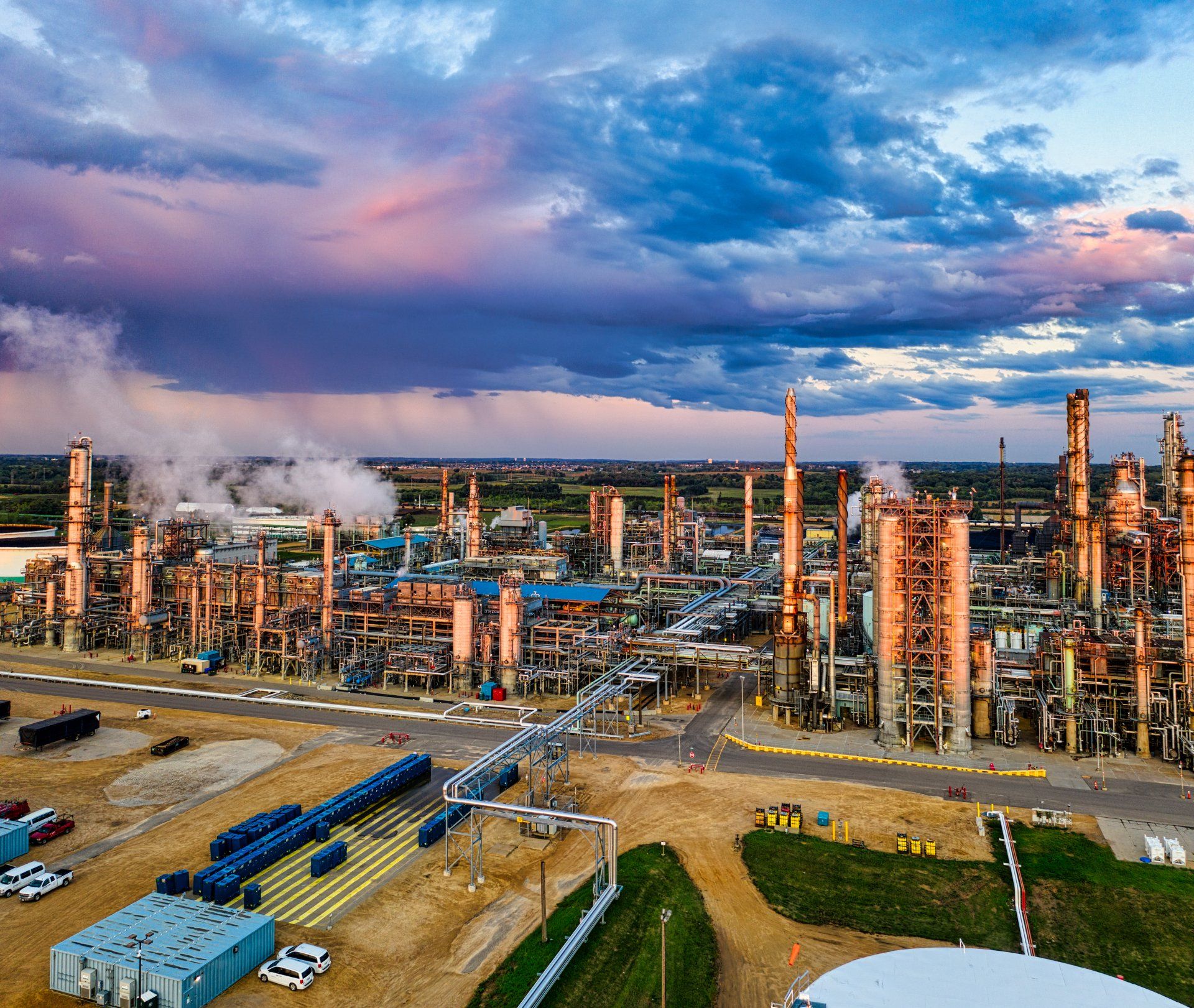 An aerial view of a large oil refinery with smoke coming out of the chimneys.