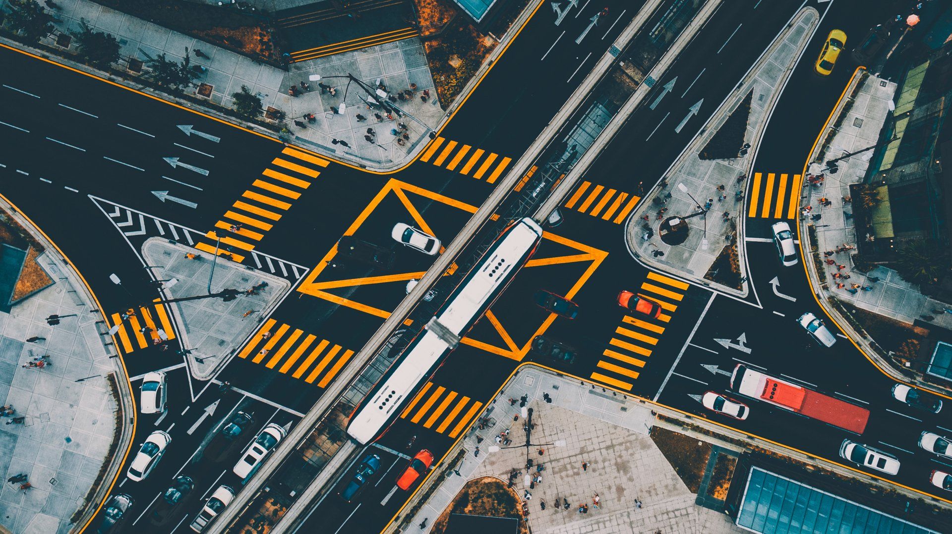 Aerial view of a busy city intersection with crosswalks, multiple lanes, and vehicles including buses, cars, and trucks.