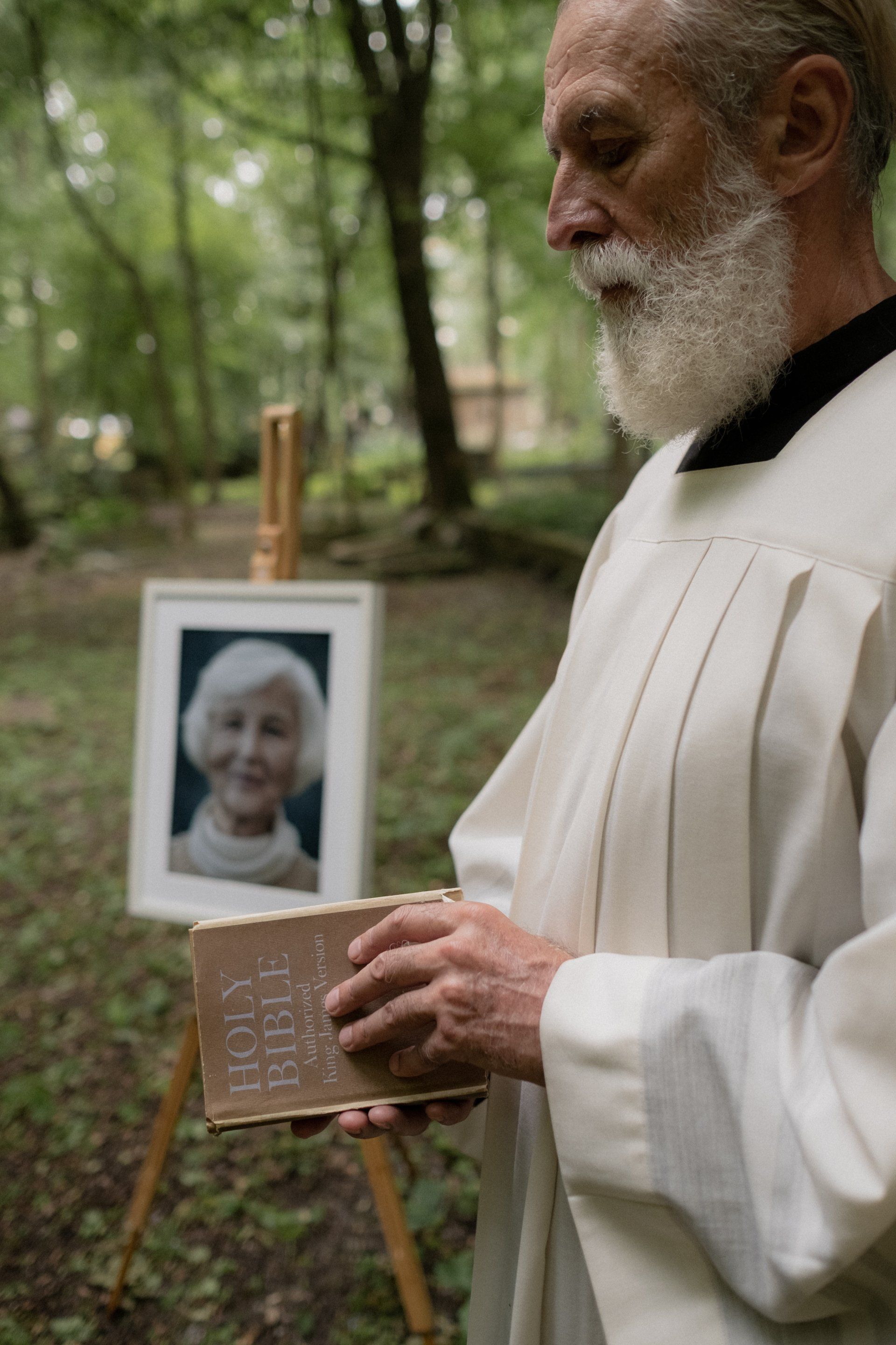 A man with a beard is holding a bible in front of a picture of an elderly woman.