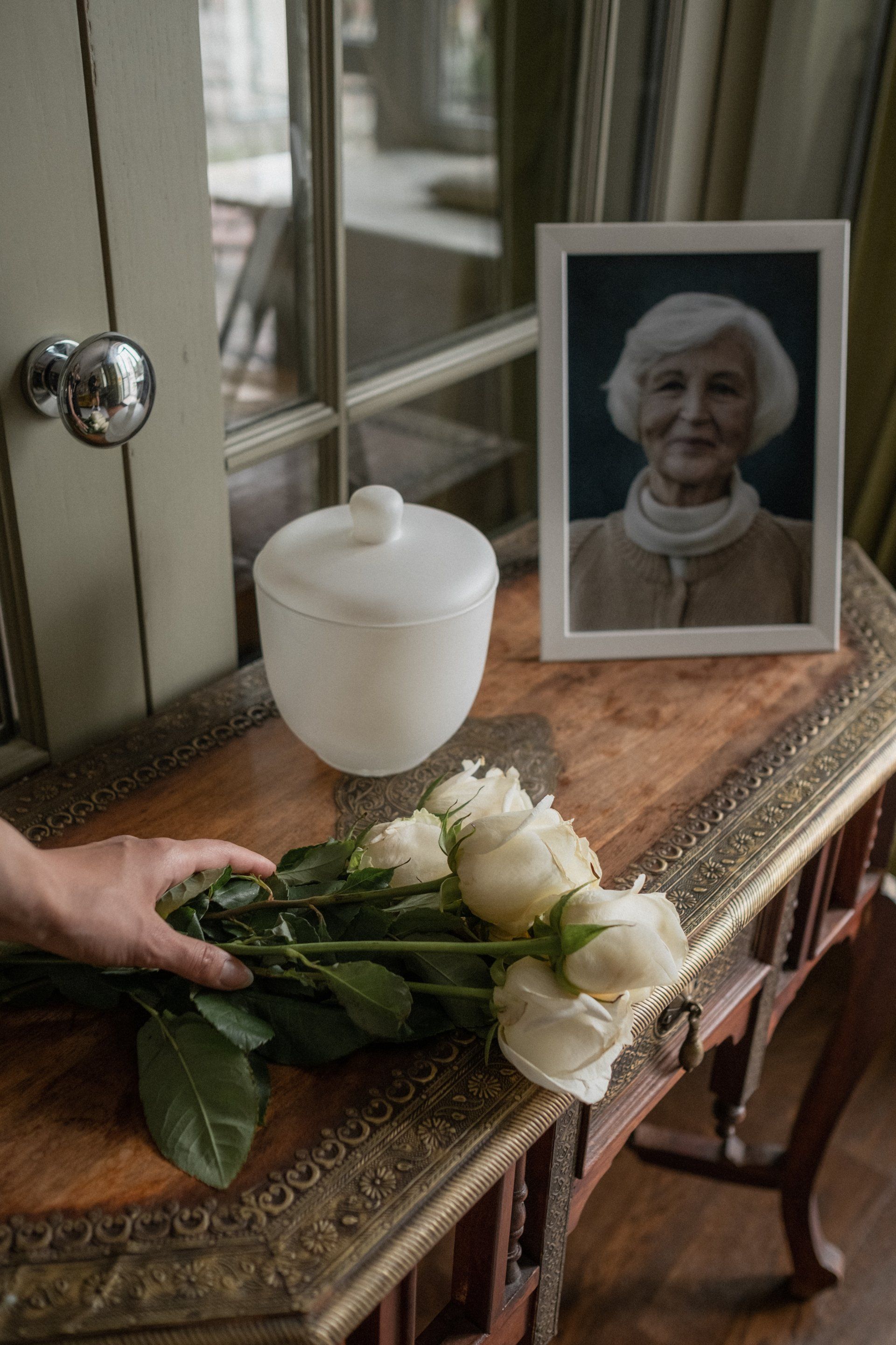 a woman holds a bouquet of white roses in front of a picture of an elderly woman