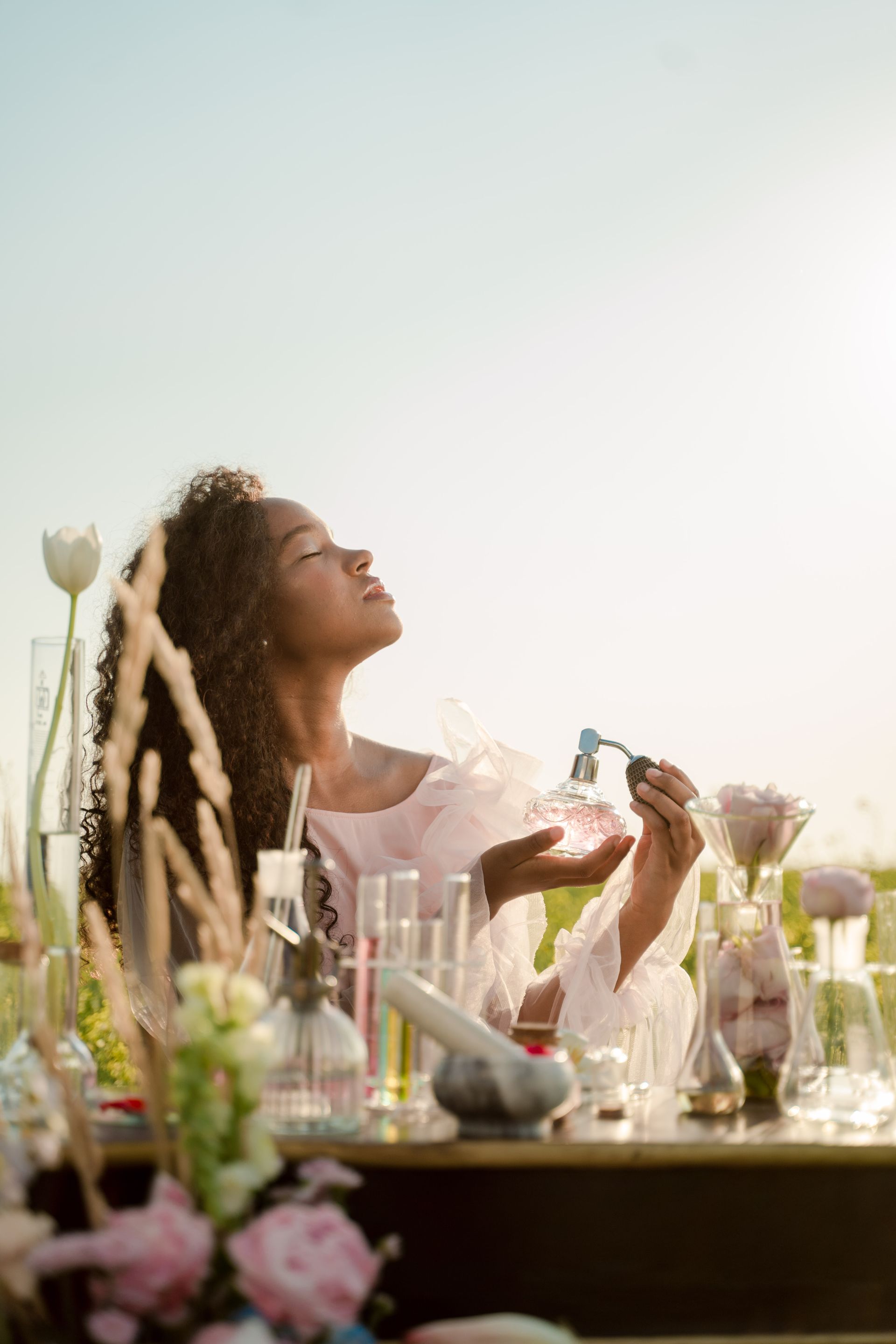 A woman is sitting at a table with a bottle of perfume in her hand.