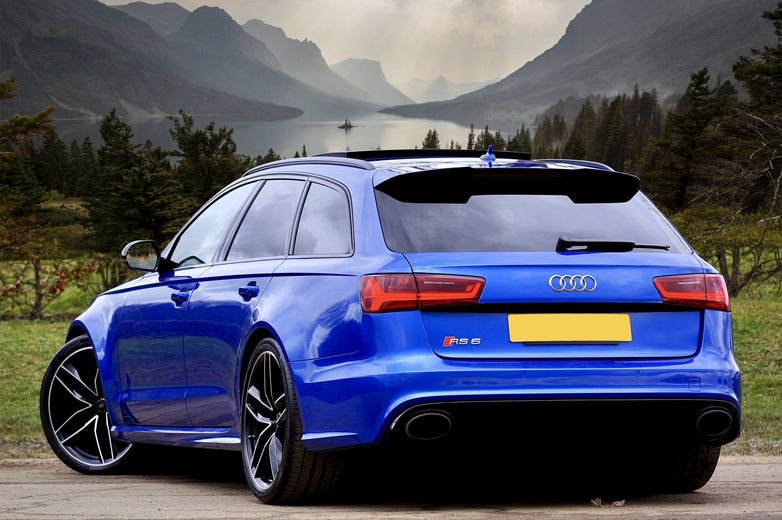 A blue audi is parked on a dirt road with mountains in the background