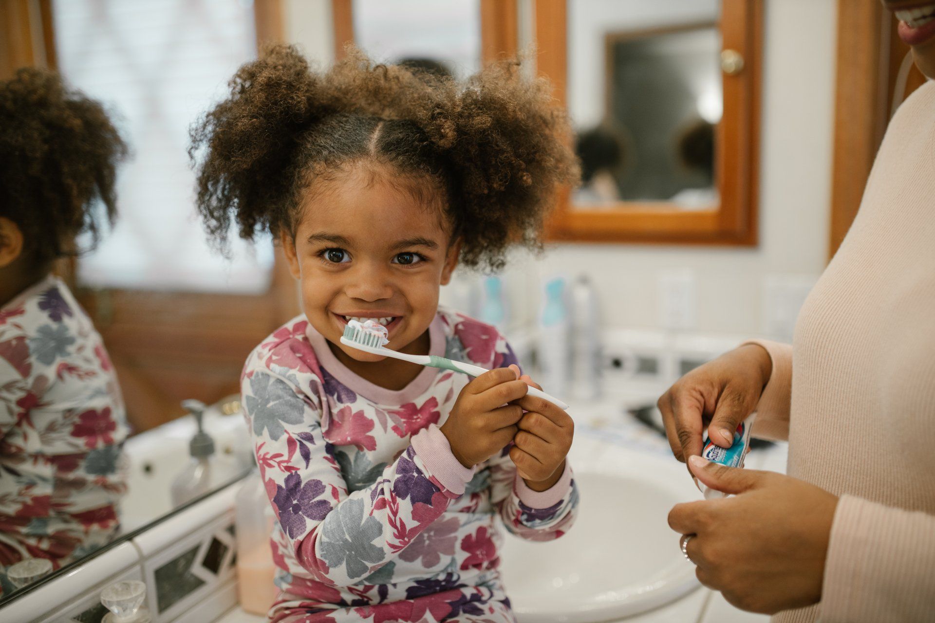 African American toddler girl brushing her teeth with her mom.