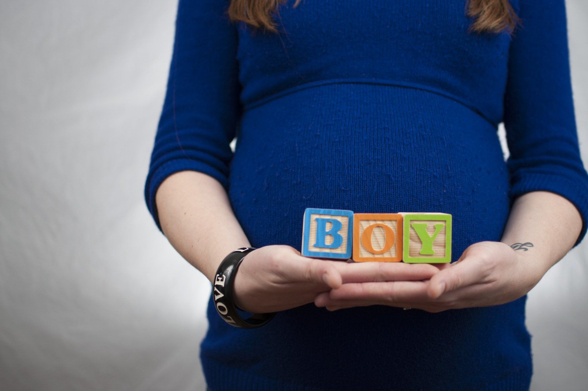 A pregnant woman holding blocks with the word boy on them