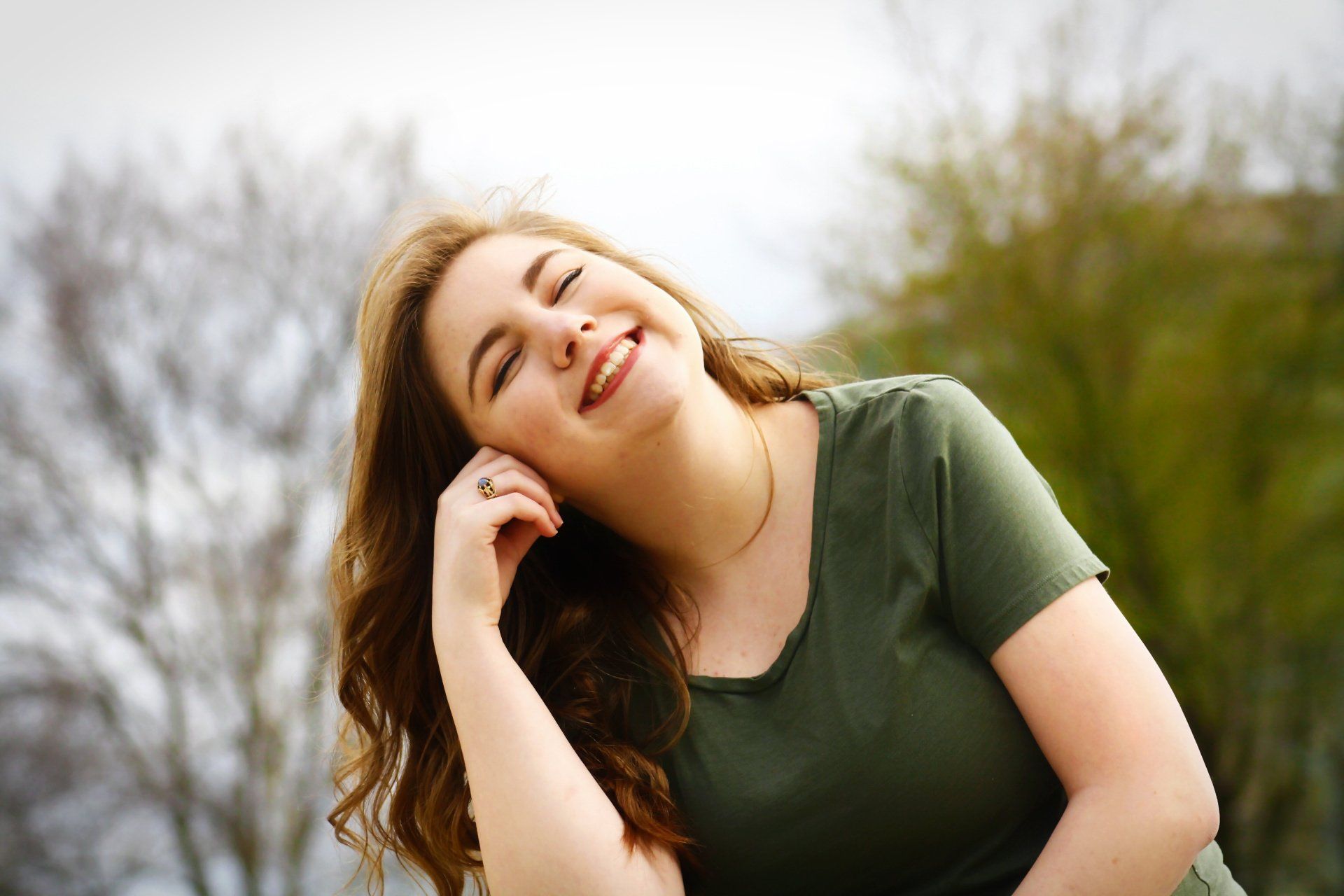 A woman in a green shirt is smiling with her eyes closed.