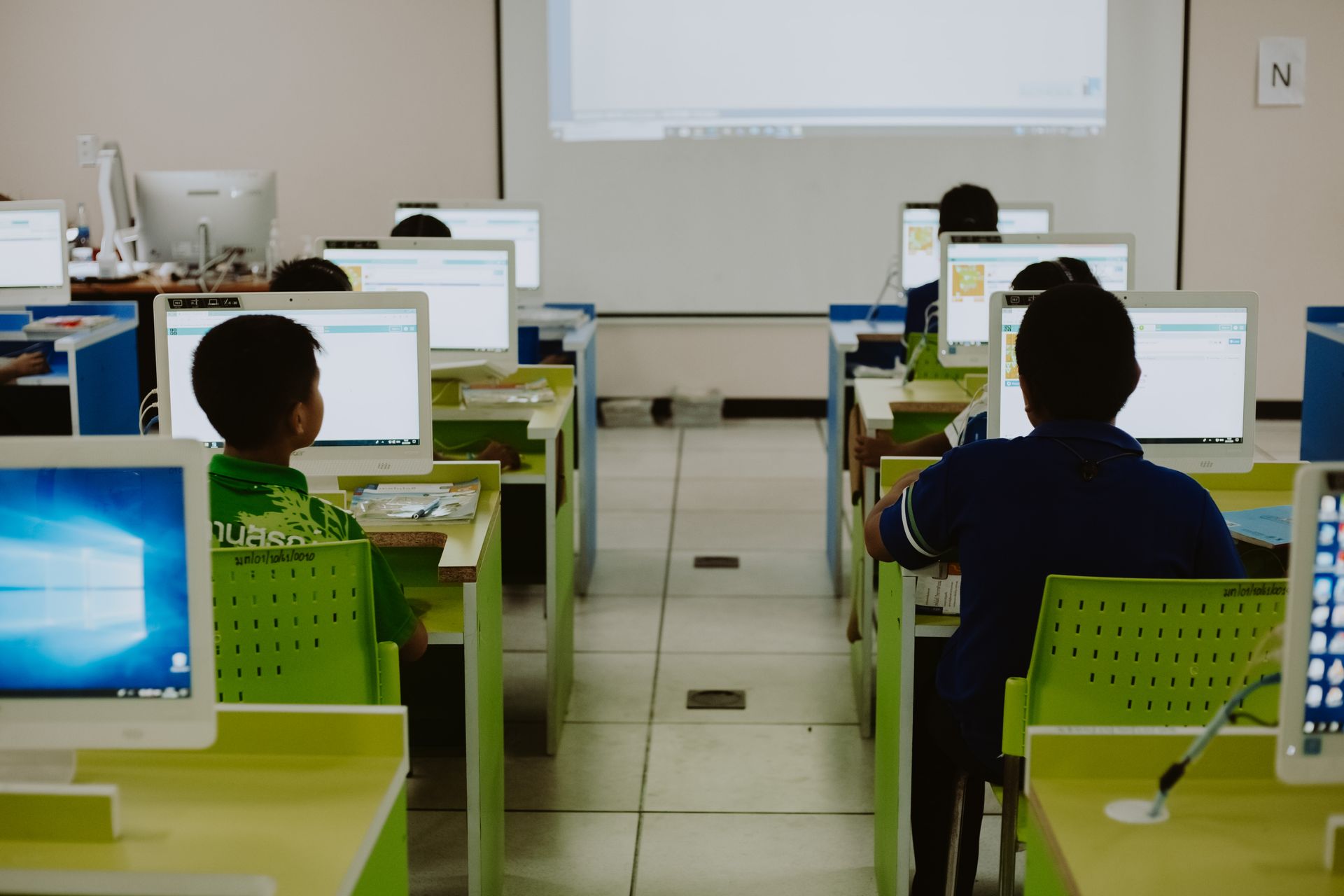 A group of children are sitting at desks in front of computer monitors in a classroom.