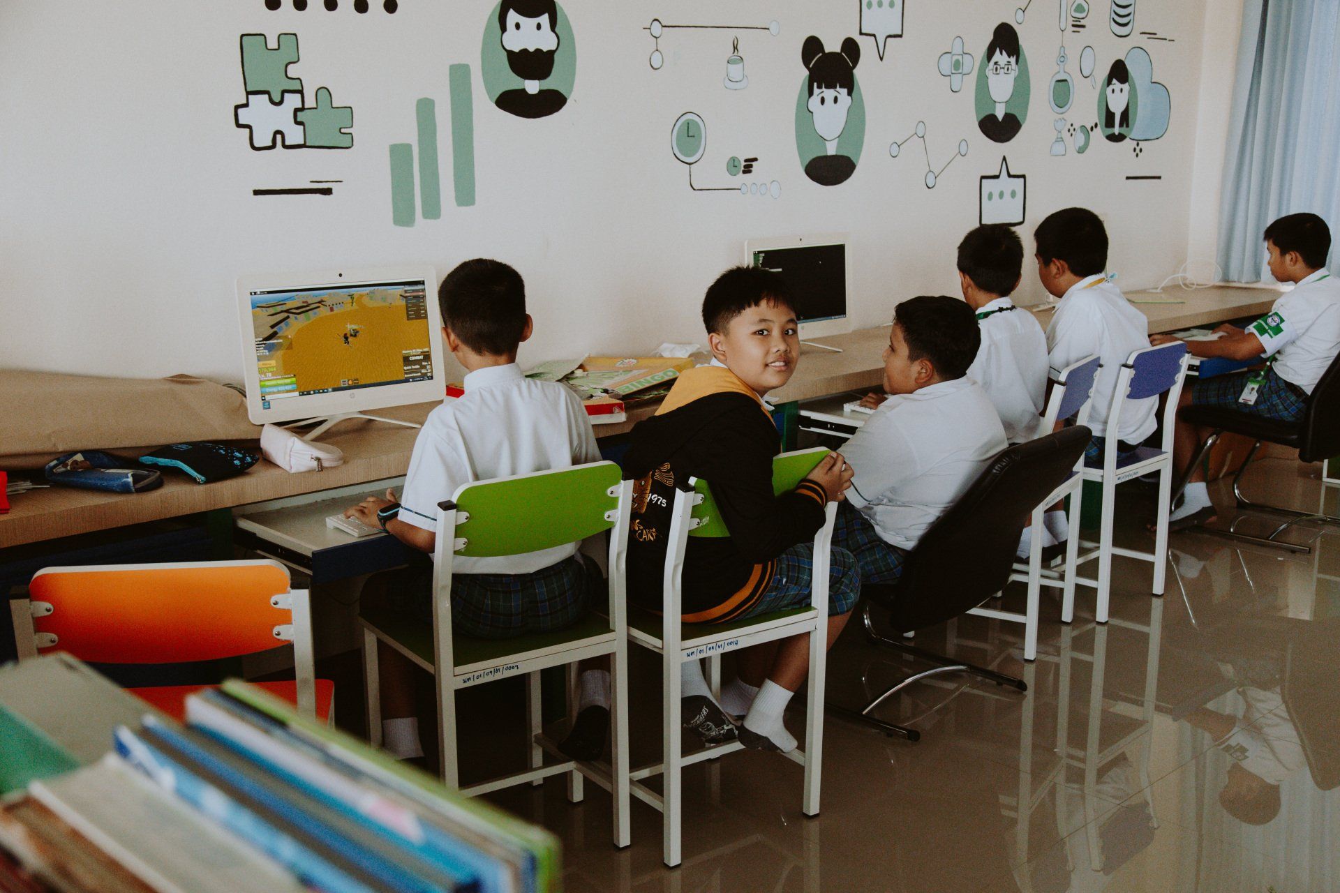 A group of children are sitting at desks in front of computers in a classroom.
