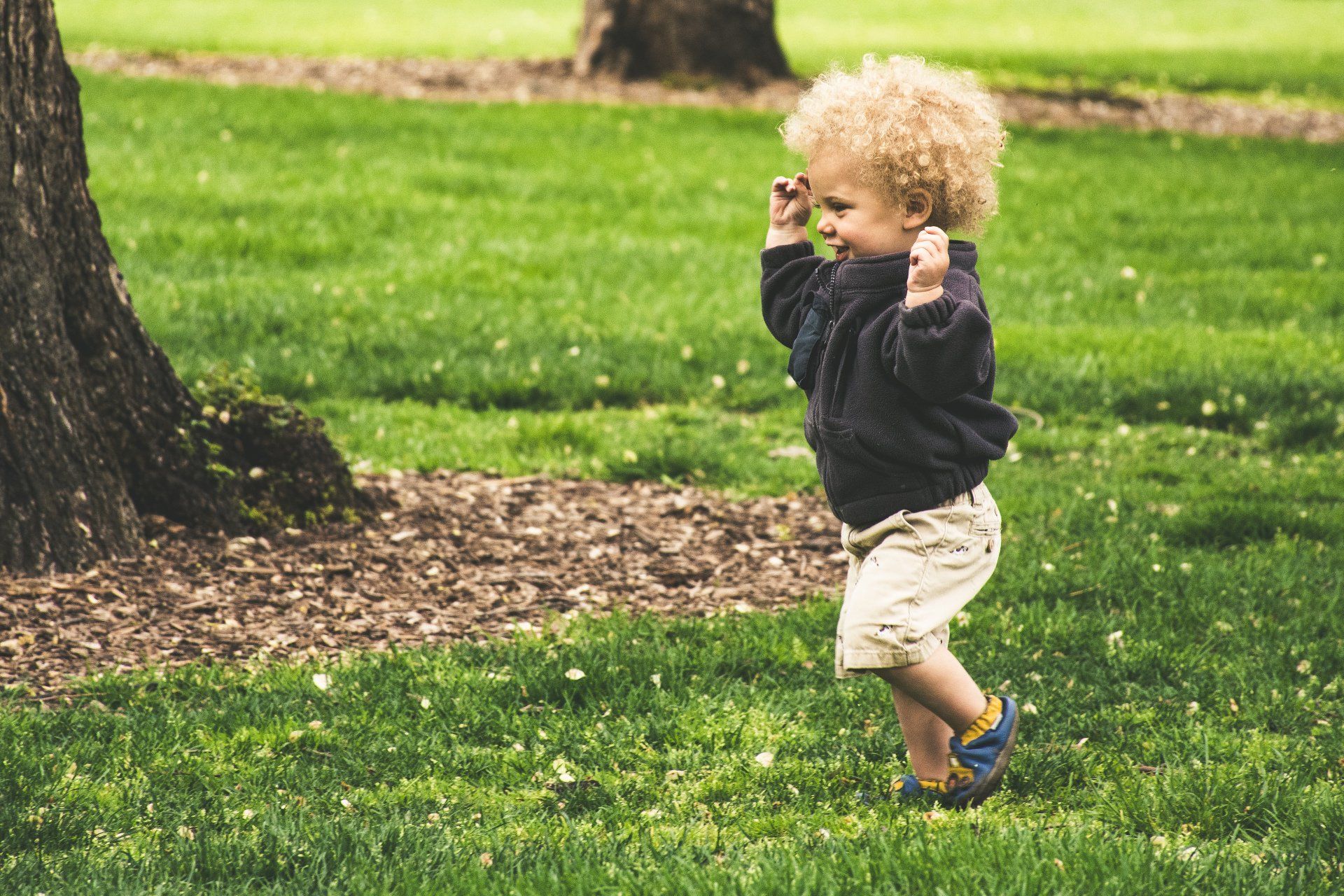 A little boy is walking in the grass in a park.