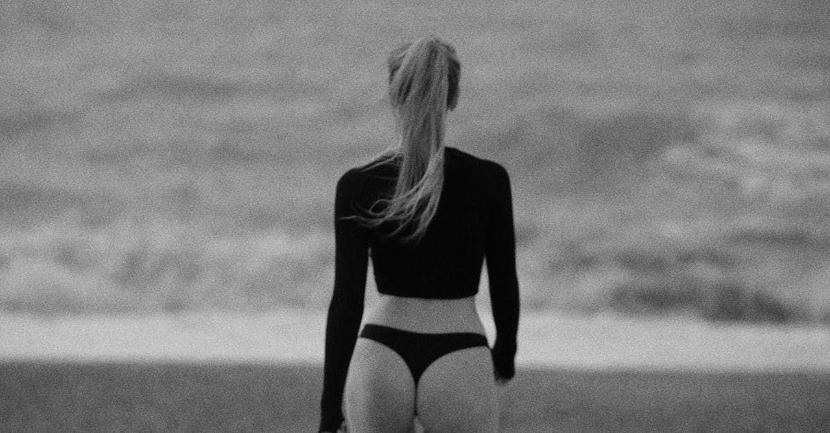 A black and white photo of a woman in a bikini walking on the beach.