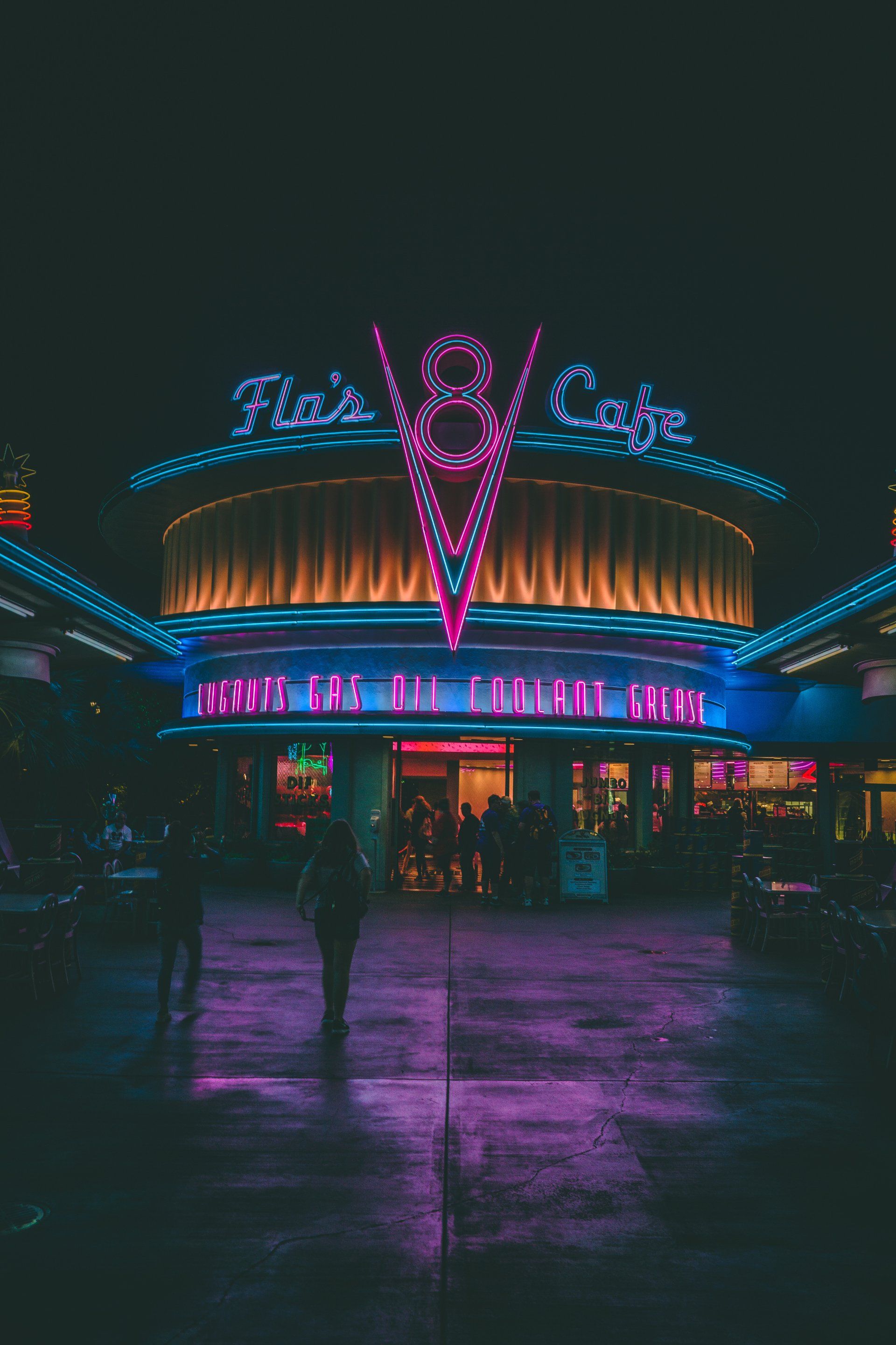 A person is walking in front of a neon lit building at night.