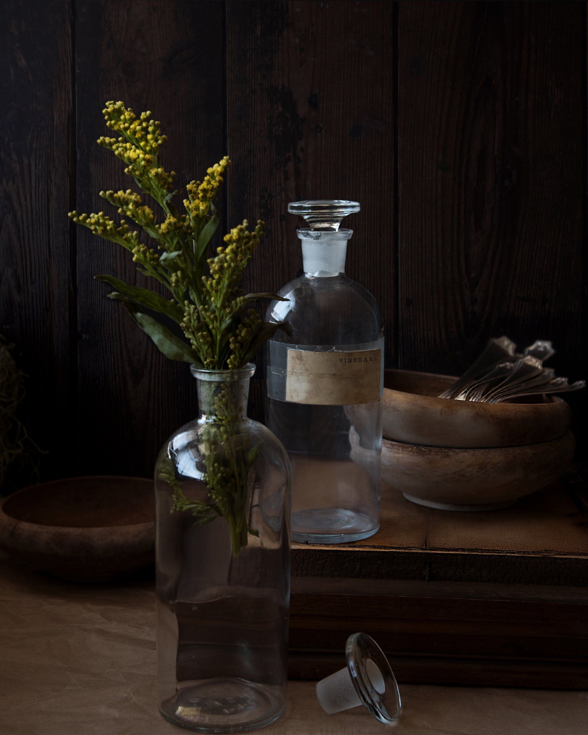 Two glass bottles with flowers in them are sitting on a wooden table.