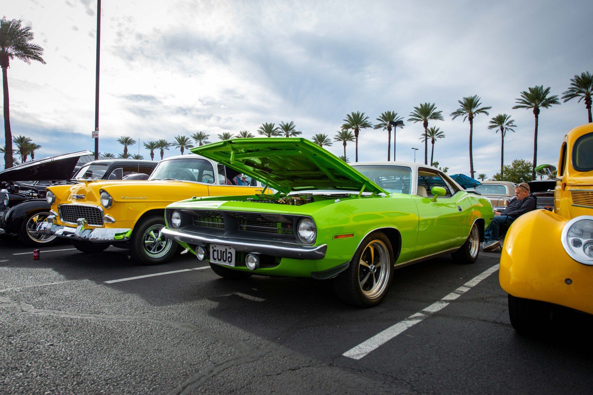 A green car with the hood up is parked next to a yellow truck.