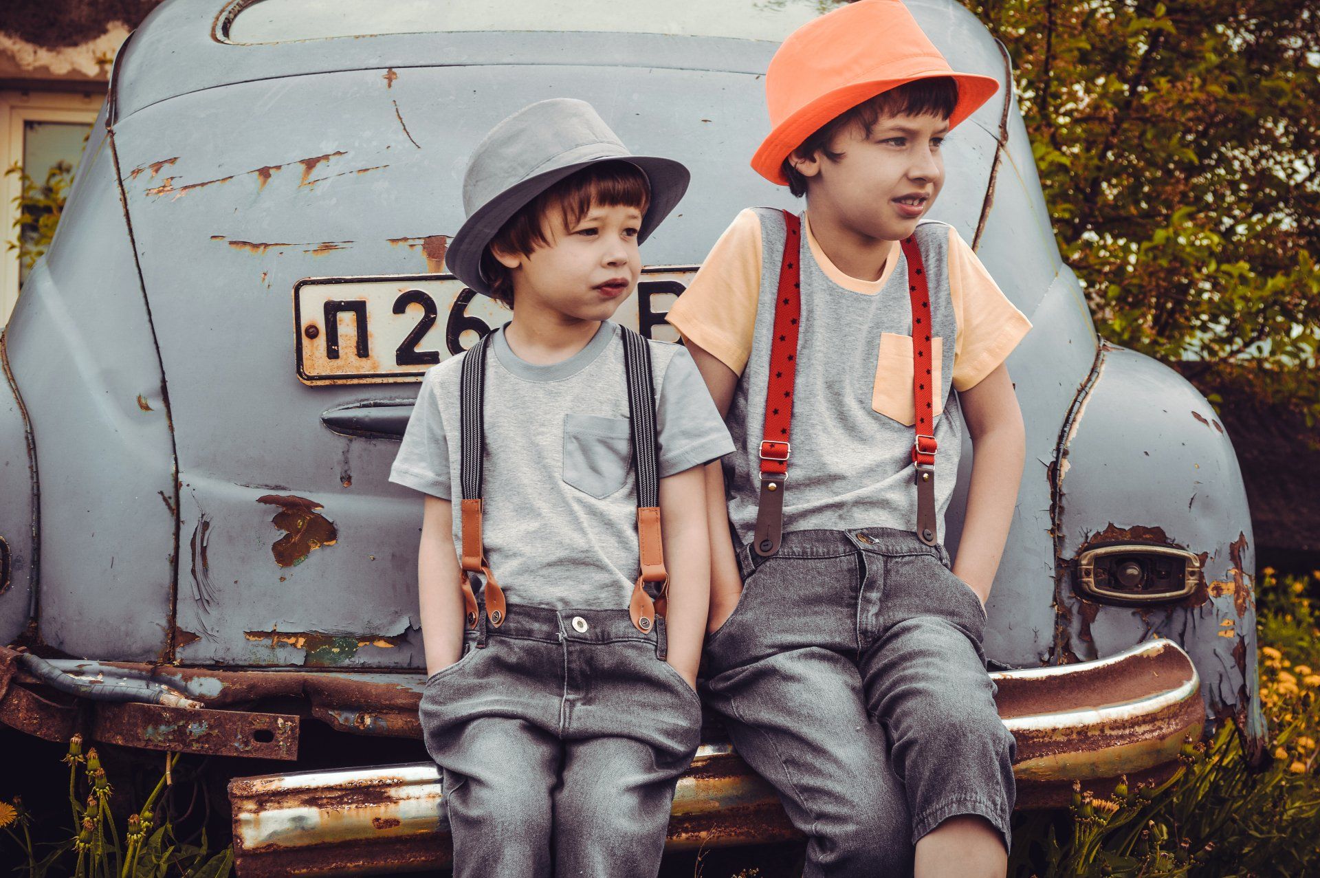two young boys are sitting on a bench in front of an old car .