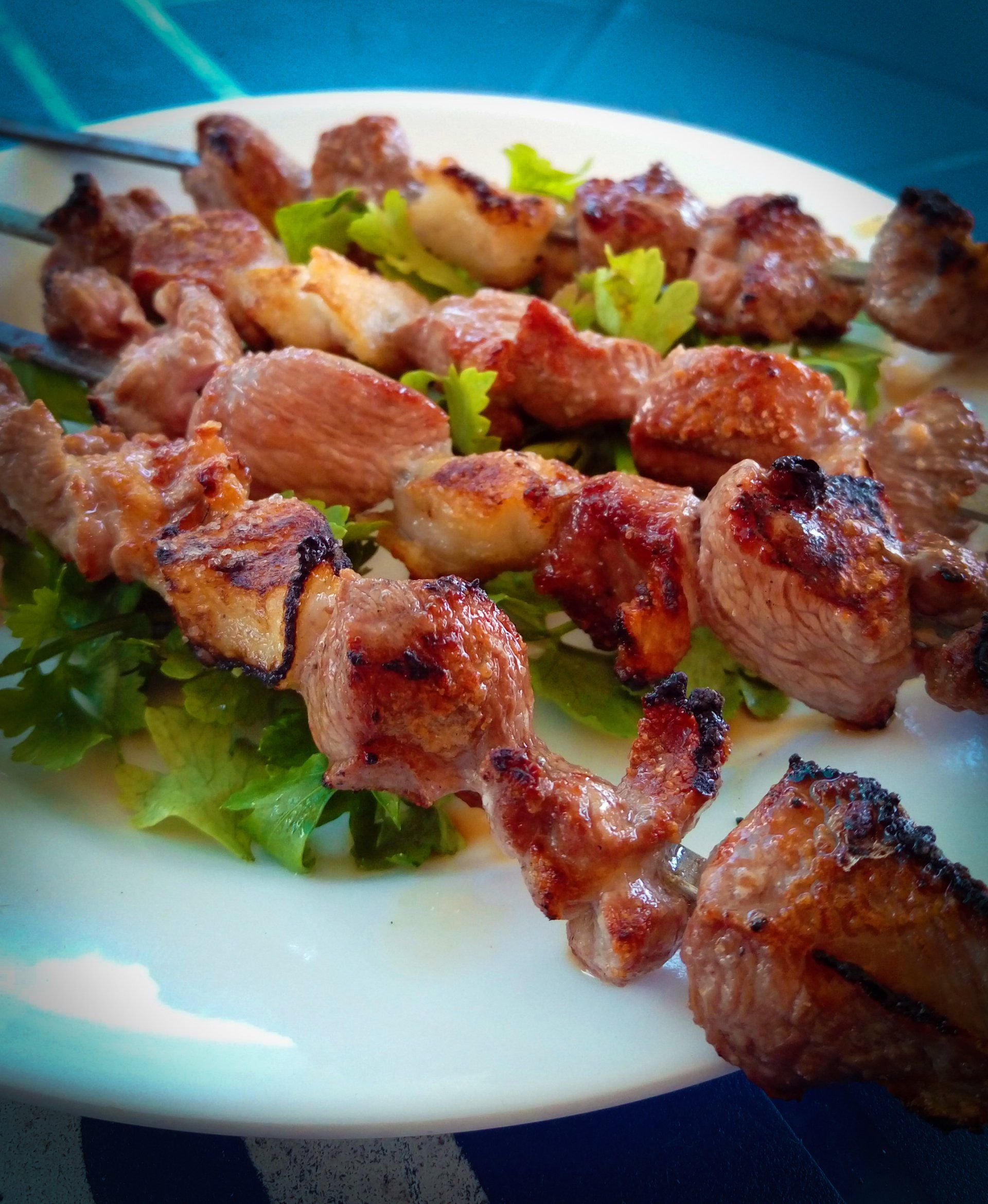 A white plate topped with meat and lettuce on skewers