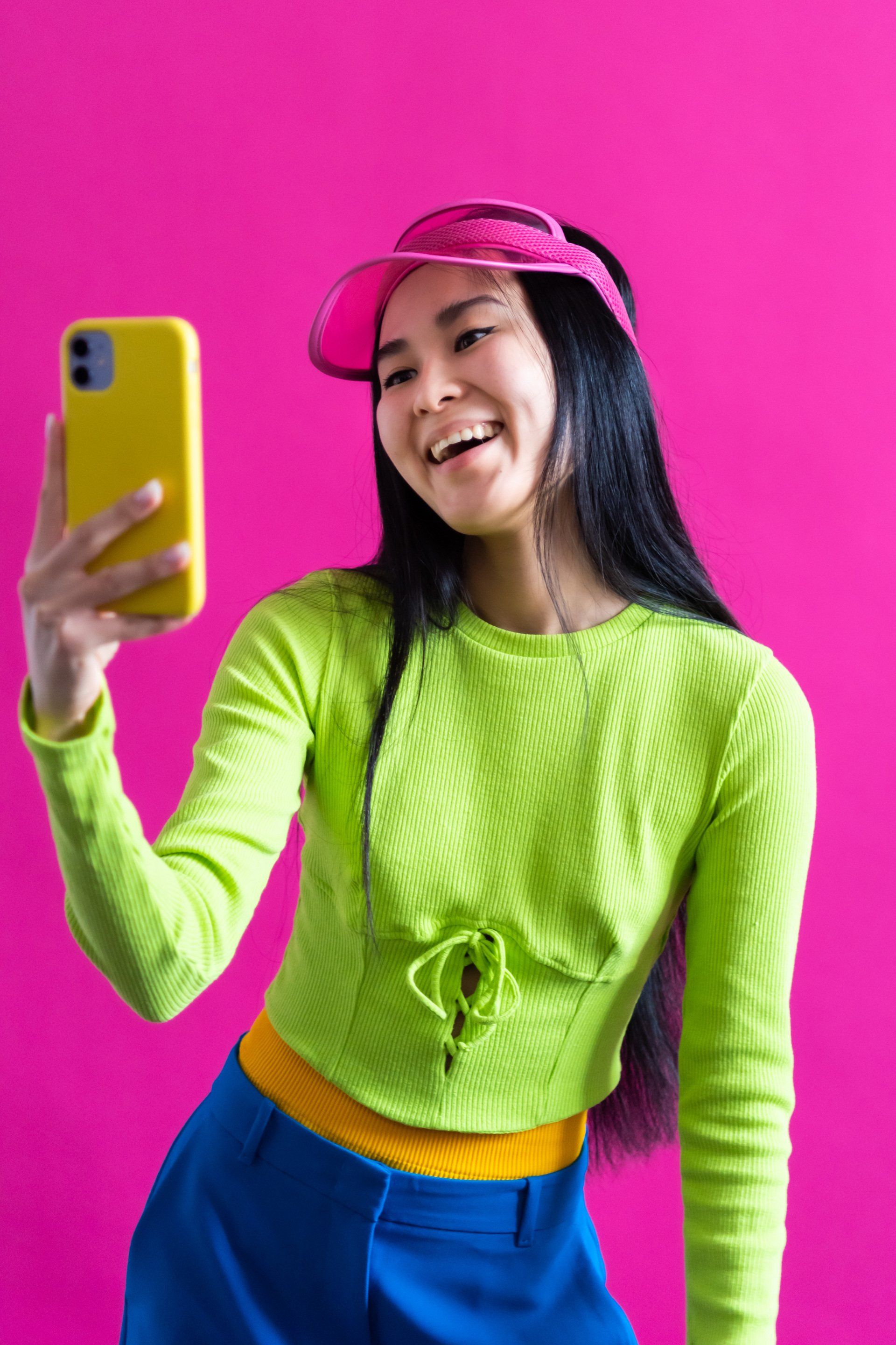Woman with pink visor taking a selfie with a yellow smart phone