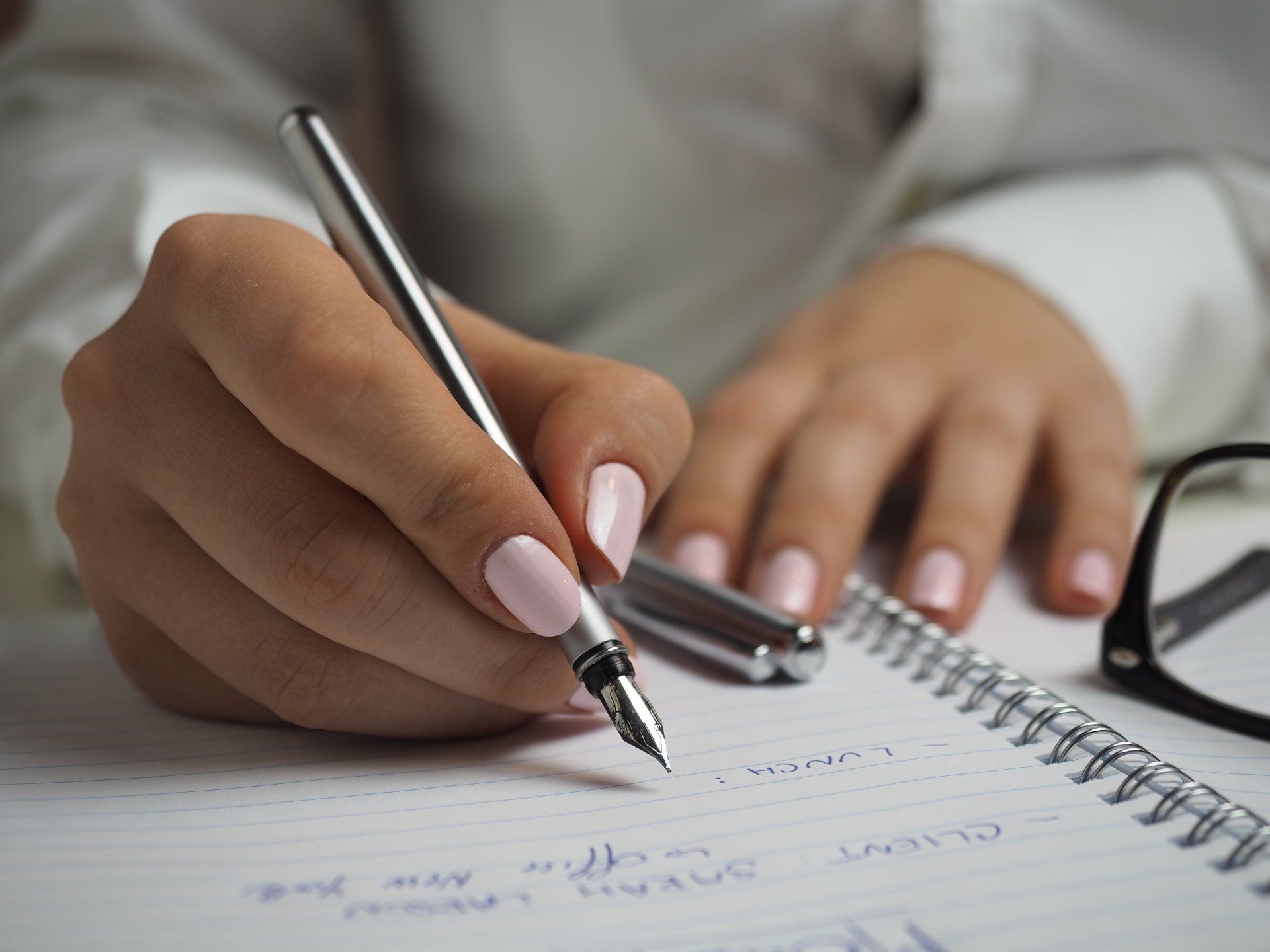 A woman is writing in a notebook with a fountain pen