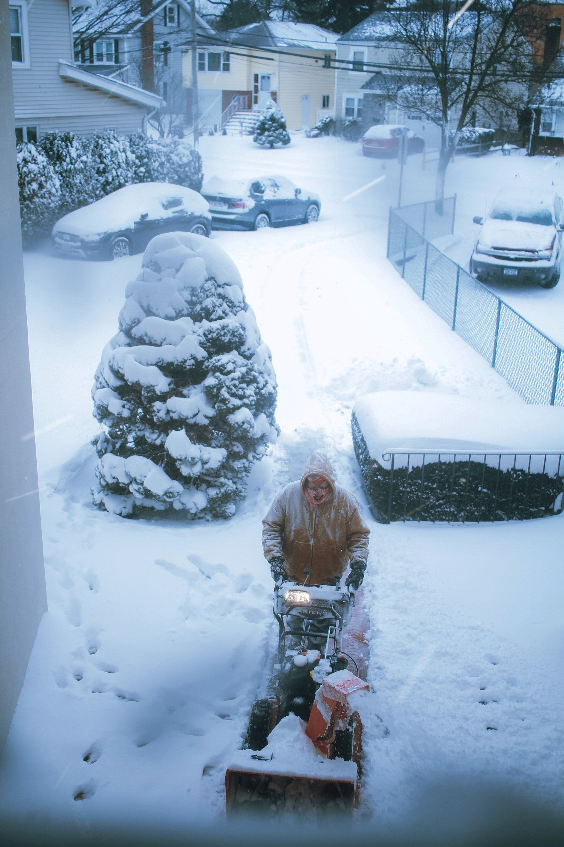 A man is using a snow blower to clear his driveway