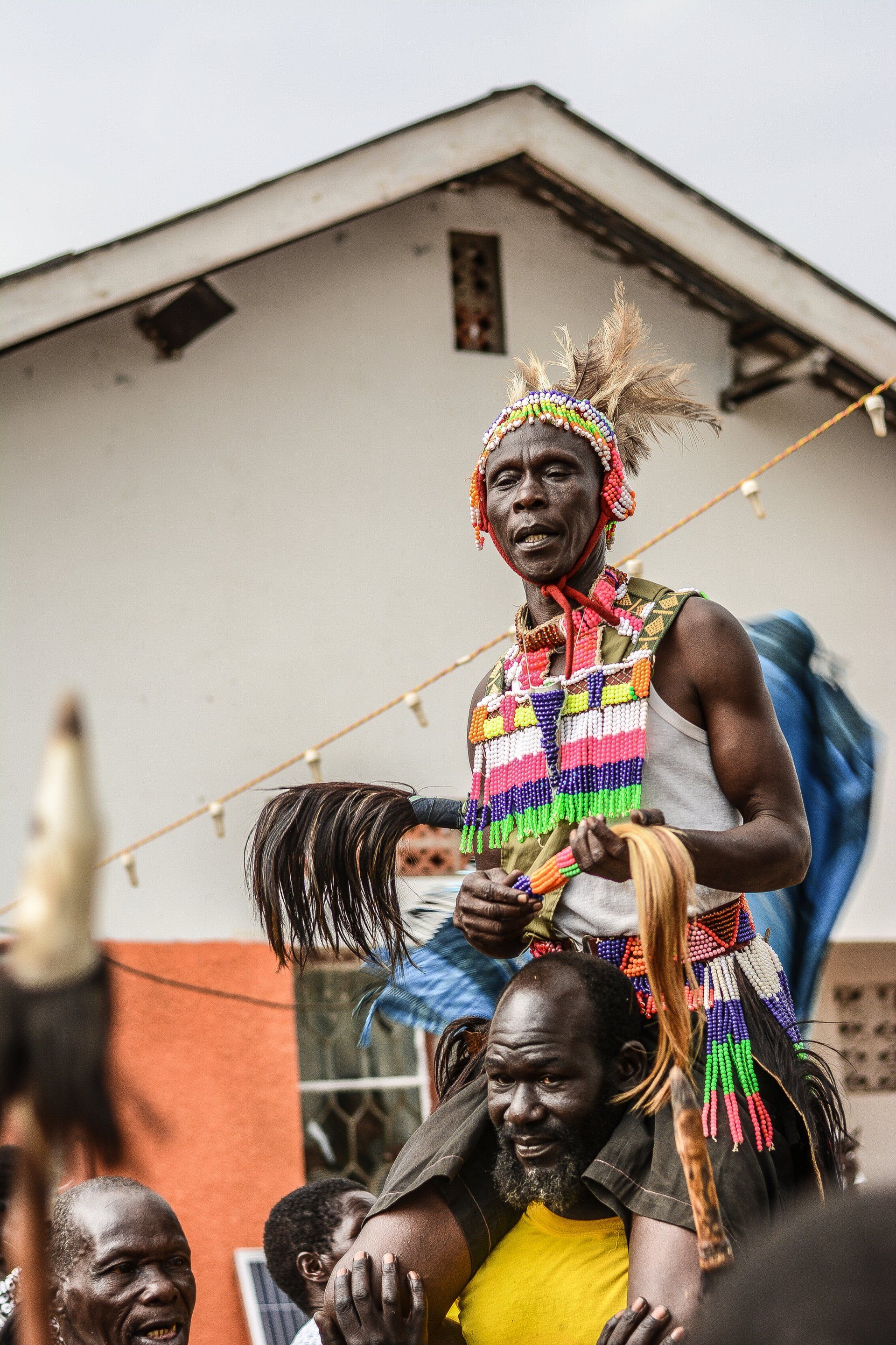 A man is carrying another man on his shoulders in front of a building.