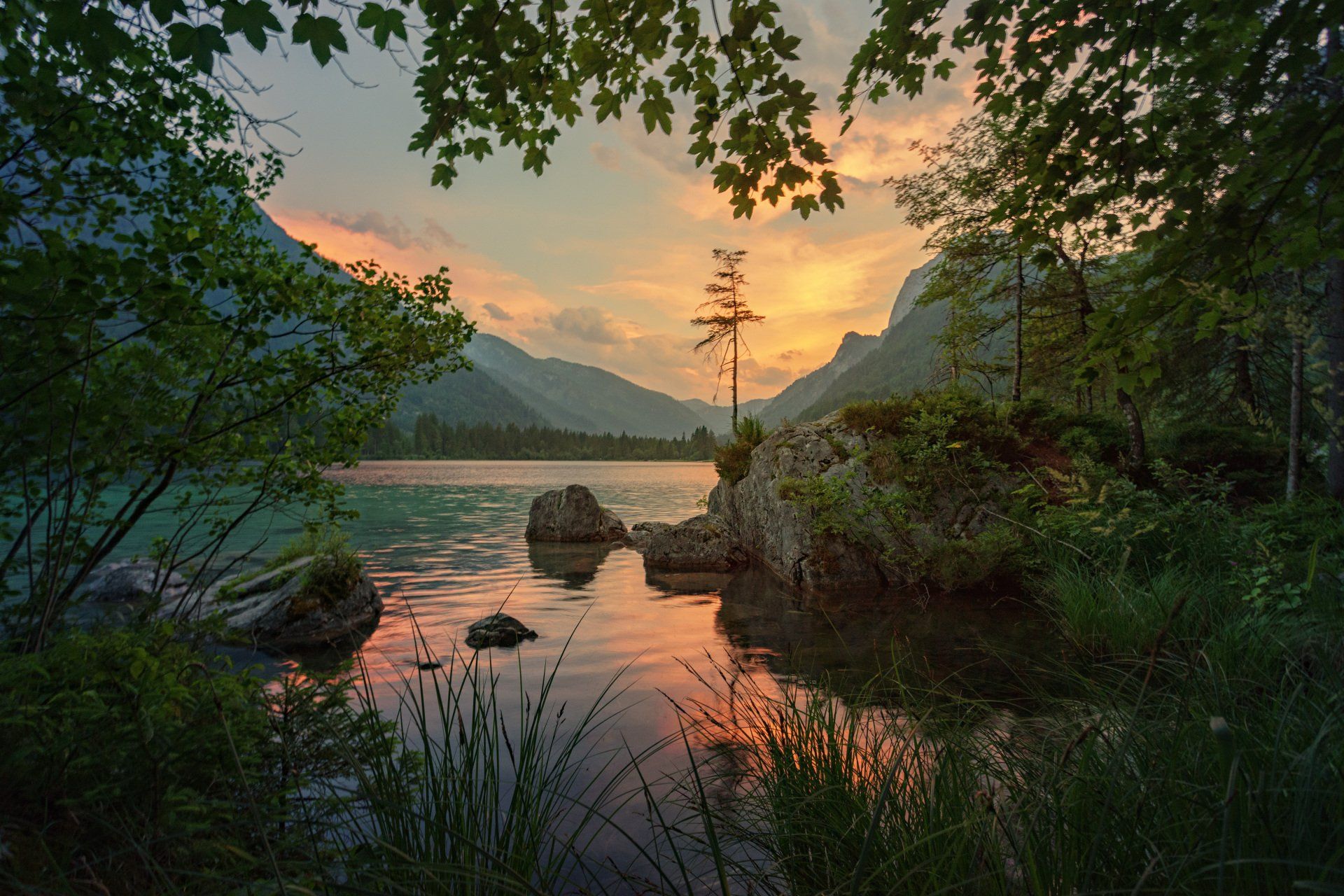 a lake surrounded by trees and mountains at sunset .