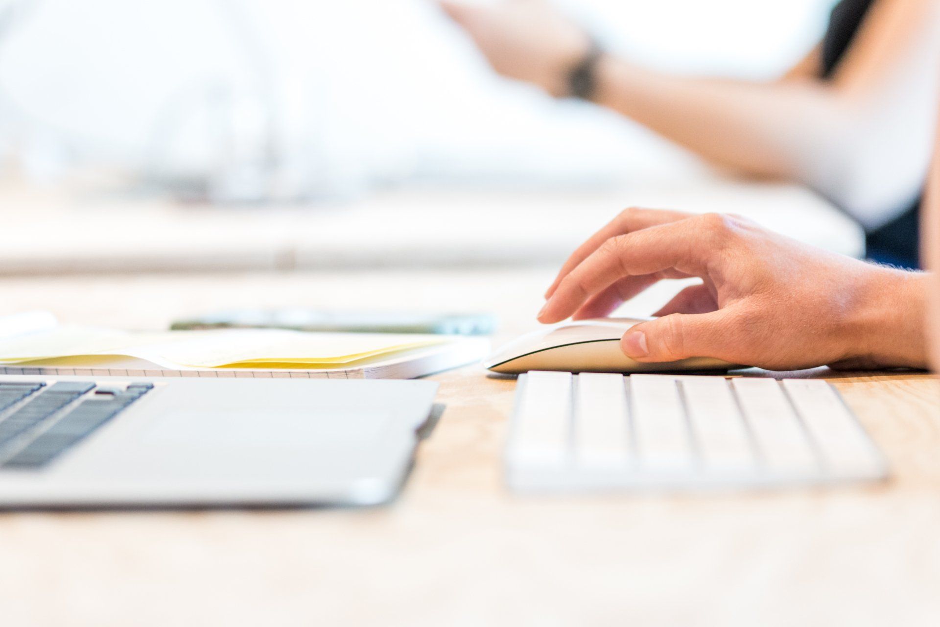 A person is typing on a keyboard next to a laptop computer.