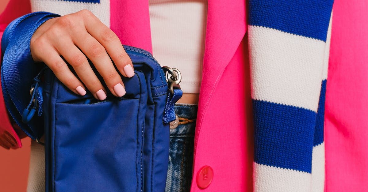 a woman in a pink jacket is holding a blue purse .