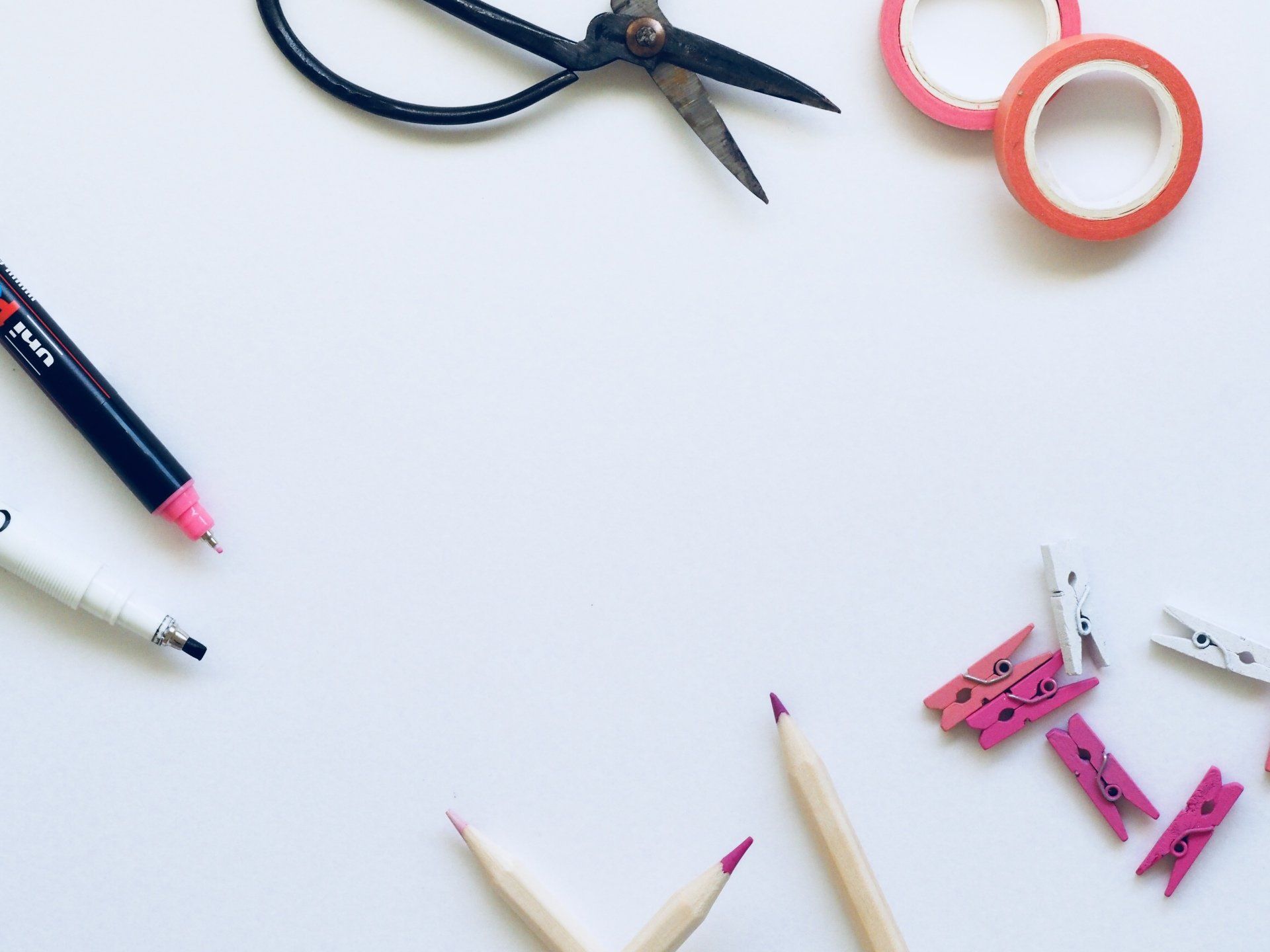 Craft supplies on white surface: scissors, tape, pens, pencils, and clothespins.