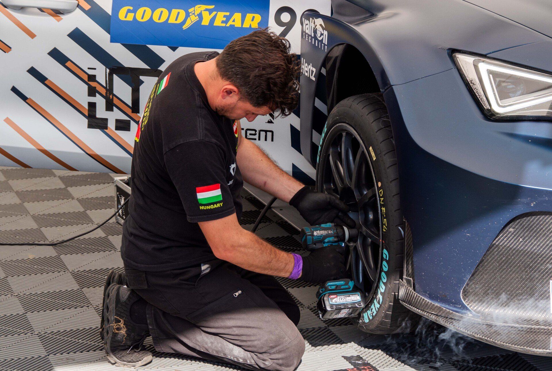 A man is kneeling down in front of a car with a good year logo on it. | Meet Your Mechanic