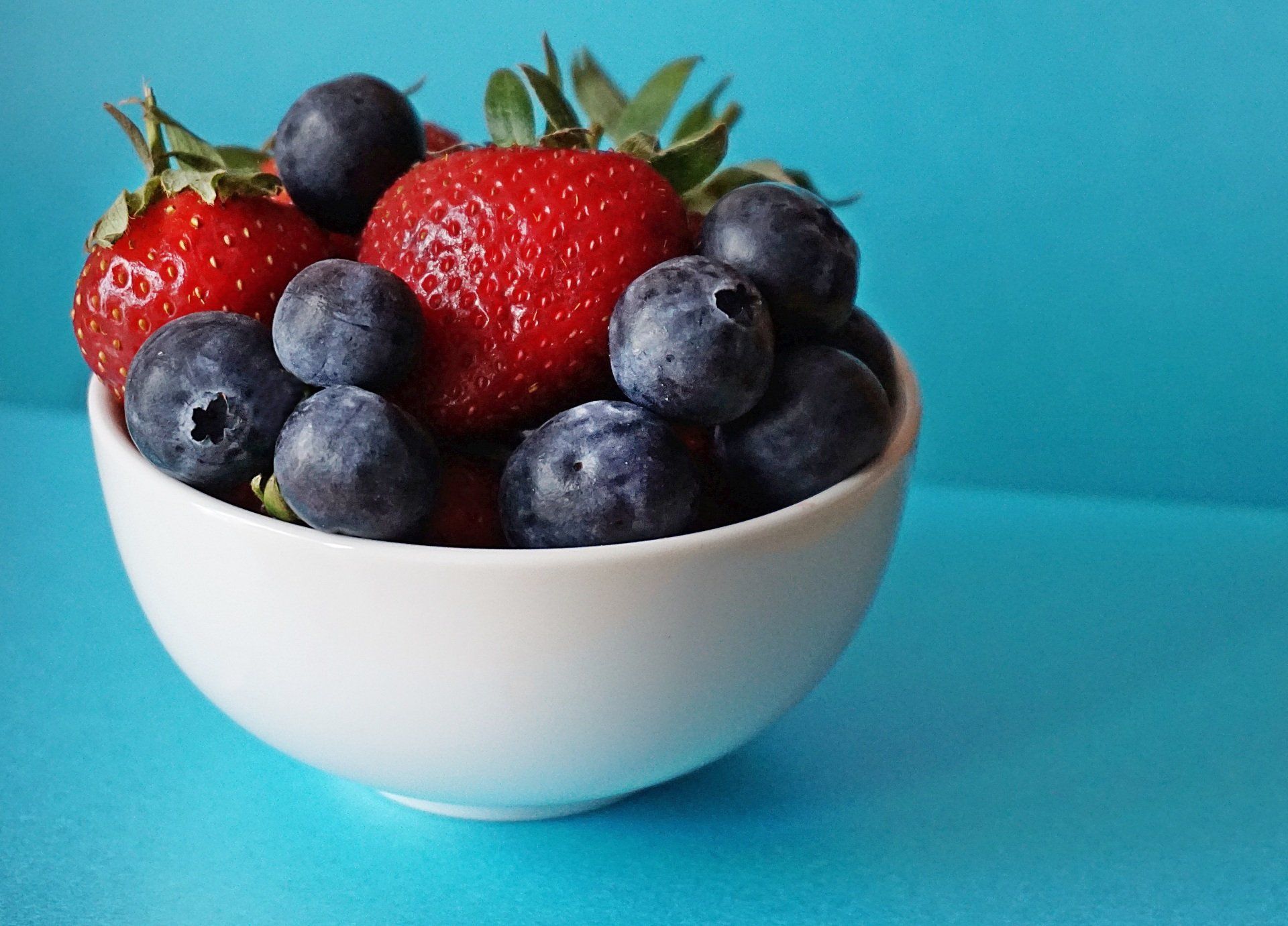 Strawberries and blueberries in a white bowl on a blue surface