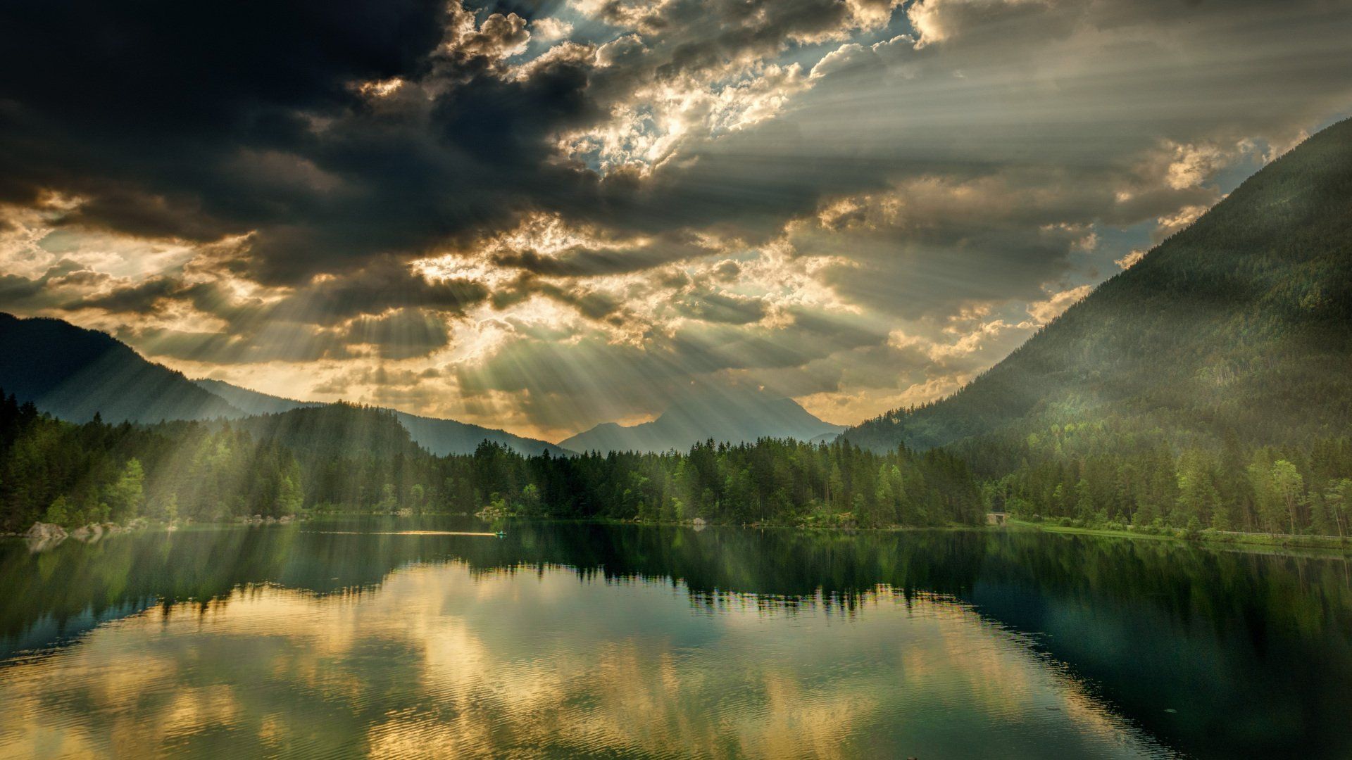 the sun is shining through the clouds over a lake surrounded by mountains .