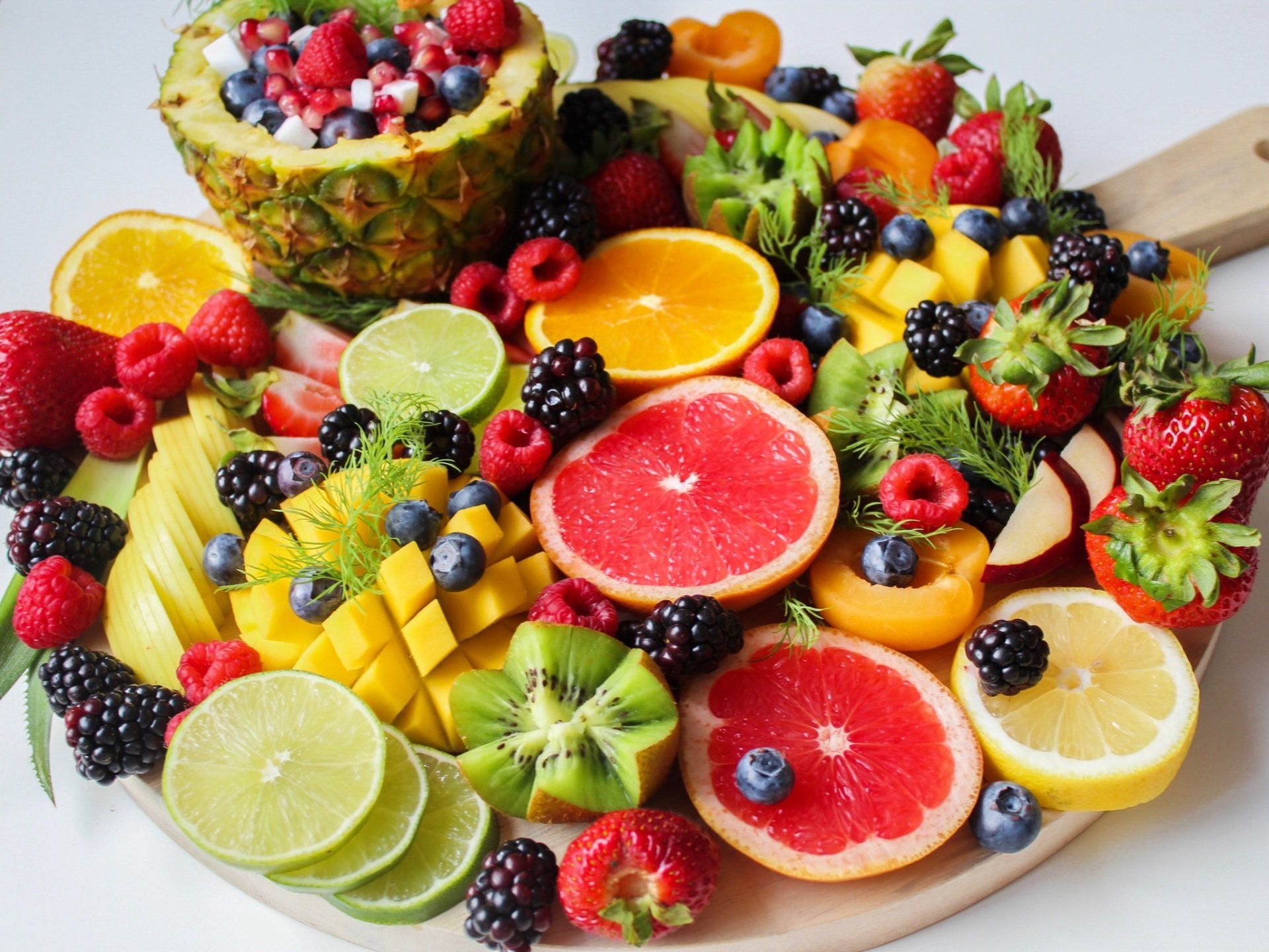 a wooden cutting board topped with a variety of fruits and berries .