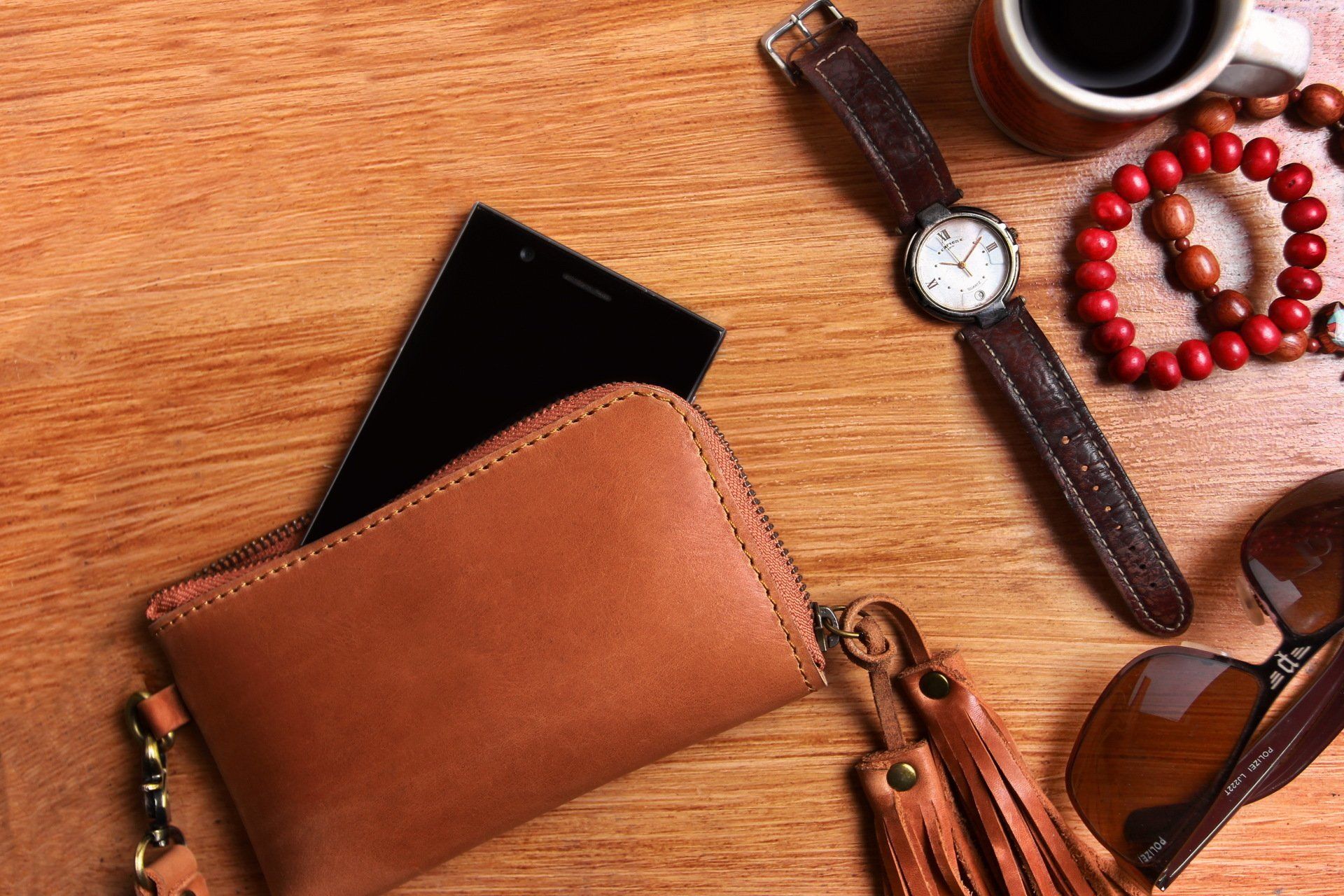 A wooden table topped with a wallet , cell phone , watch , sunglasses and a cup of coffee.