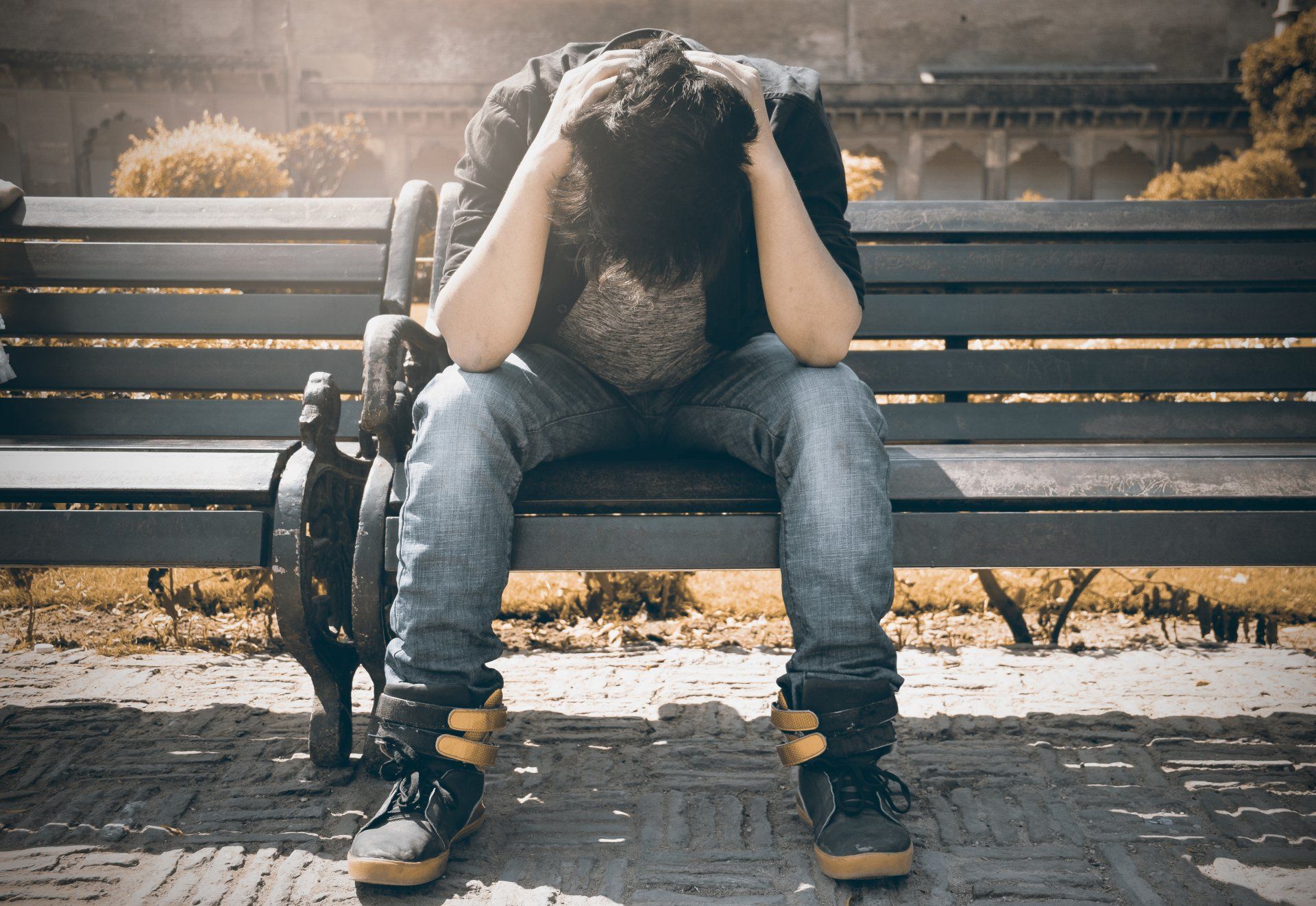 a man sits on a bench with head in hands and elbows on thighs