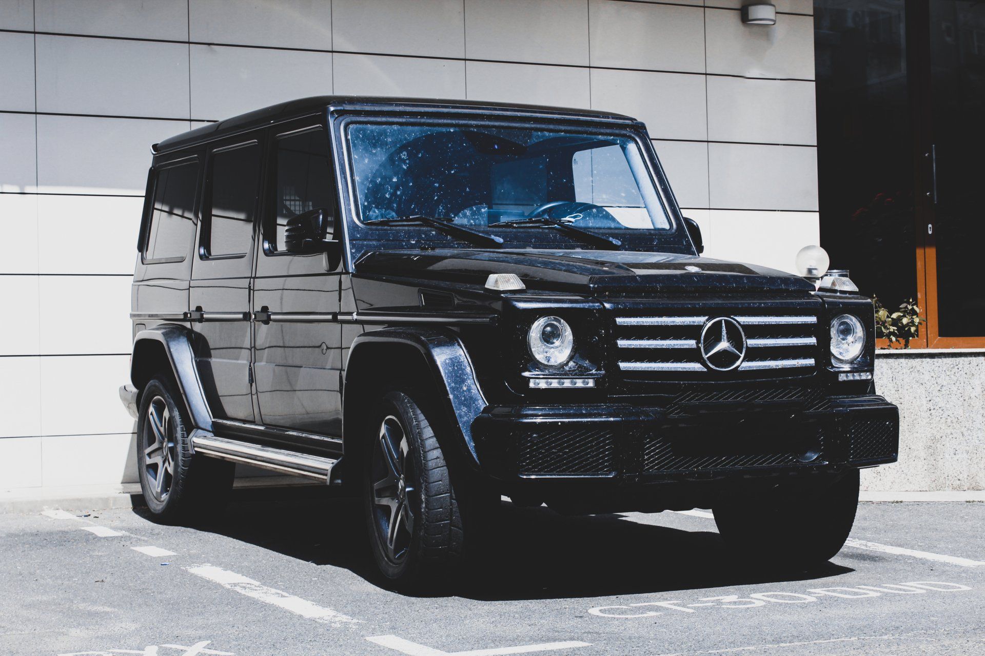 A black mercedes is parked in a parking lot in front of a building.