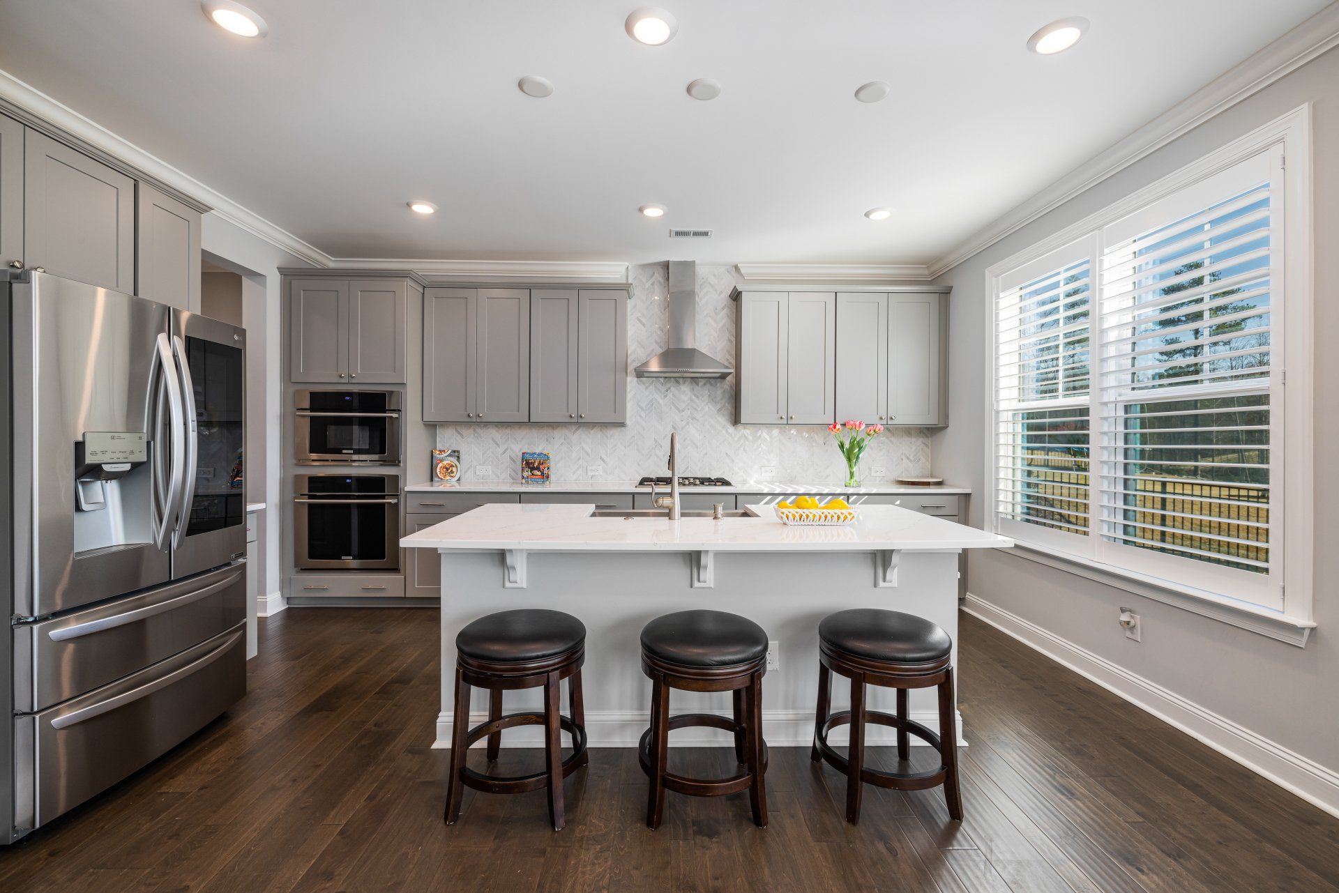 A modern kitchen with gray cabinets, marble counter and backsplash, and recessed lighting