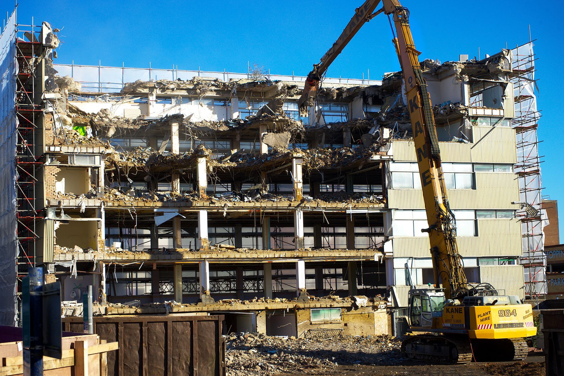 A large building is being demolished by a yellow excavator.