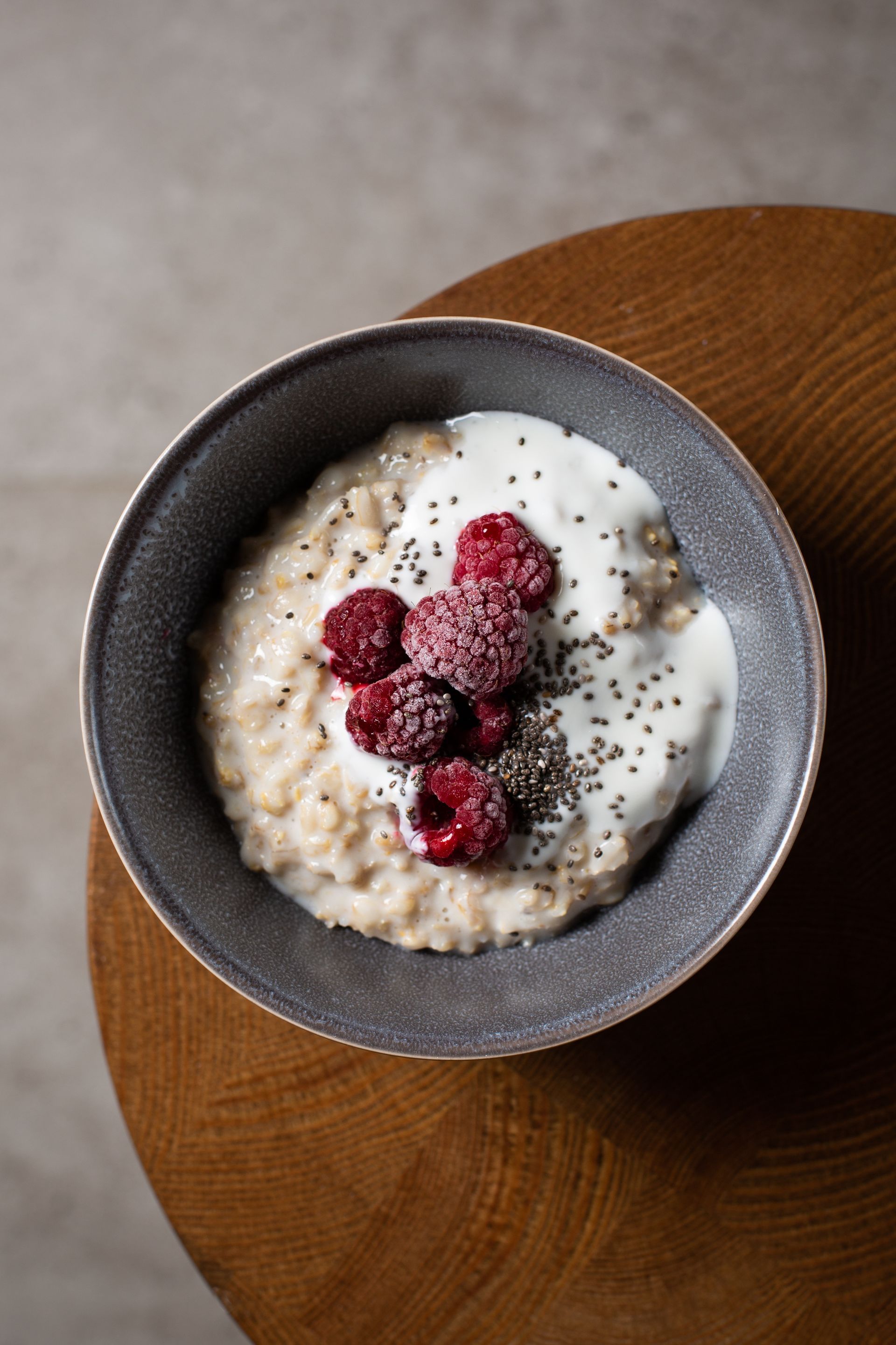 A bowl of oatmeal with raspberries and yogurt on a wooden table.