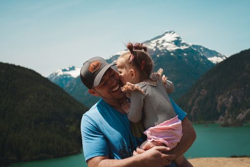 A man is holding a little girl in his arms in front of a lake.
