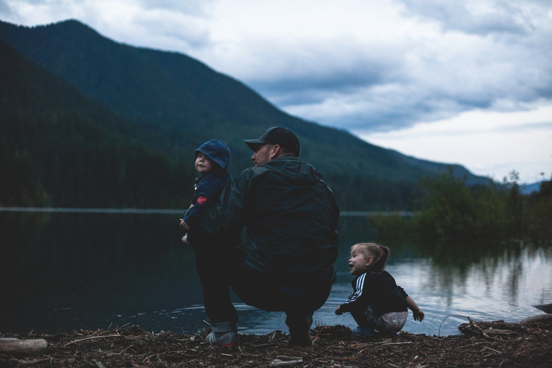 A man and two children are sitting on the shore of a lake.