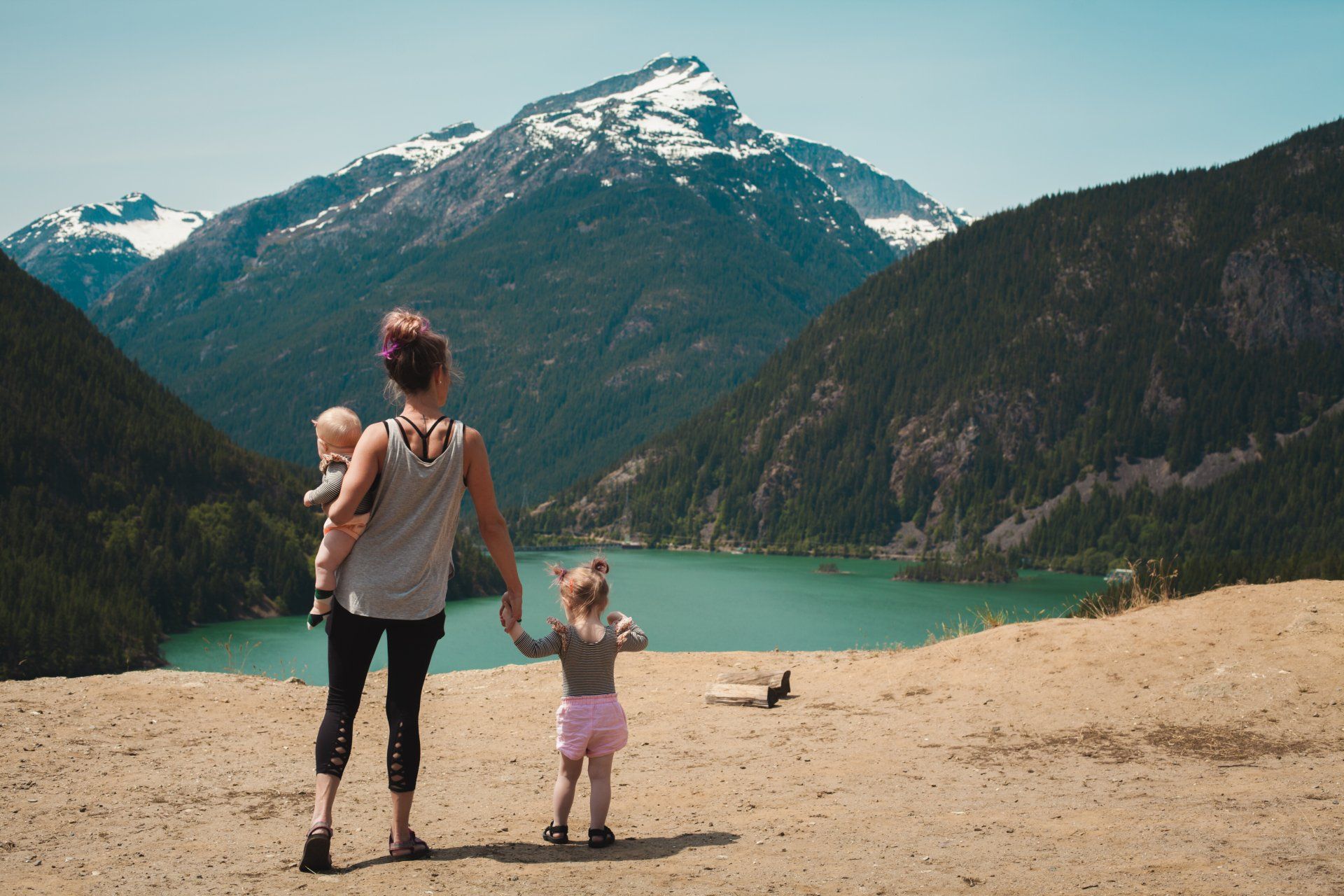 a woman is holding a baby and a little girl while standing on top of a hill overlooking a lake .