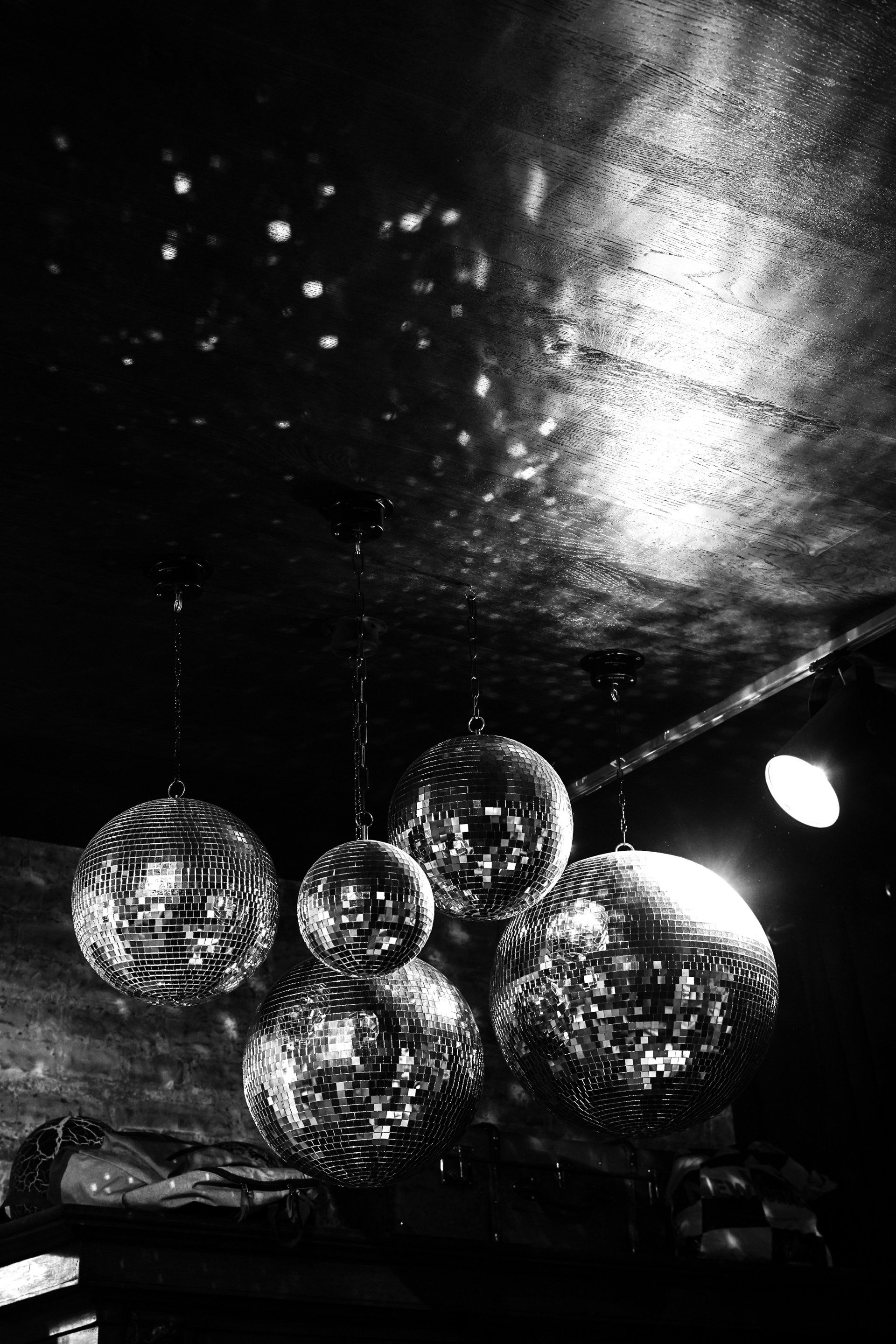 Five disco balls hanging from a dark ceiling, reflecting light.