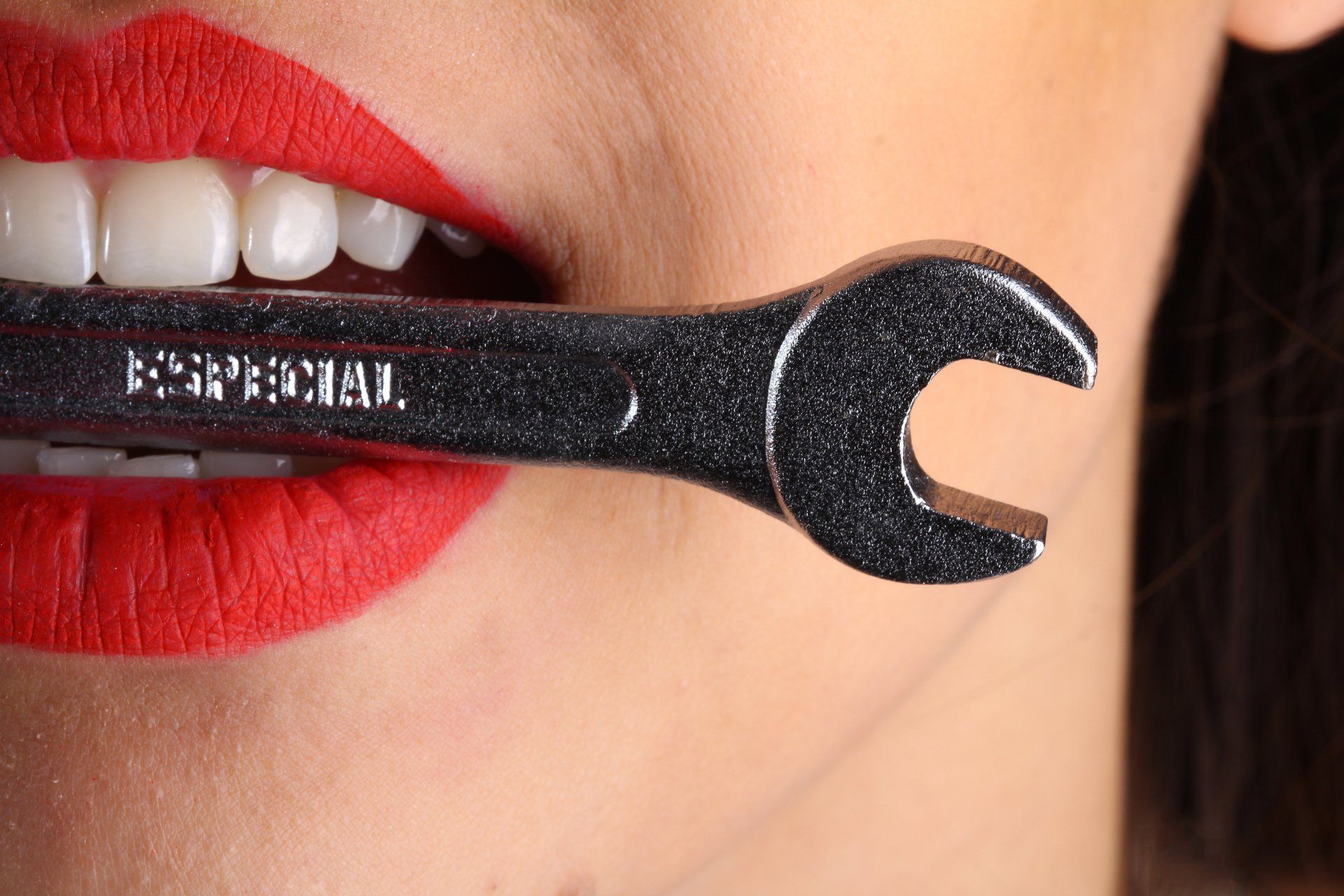 woman's face with red lipstick and a wrench in her mouth
