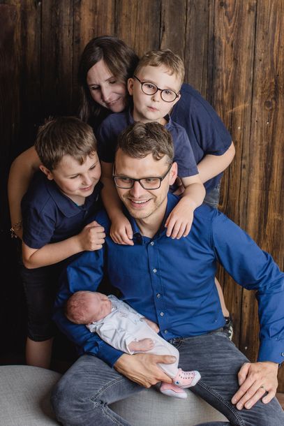 A man is holding a newborn baby while his family looks on.
